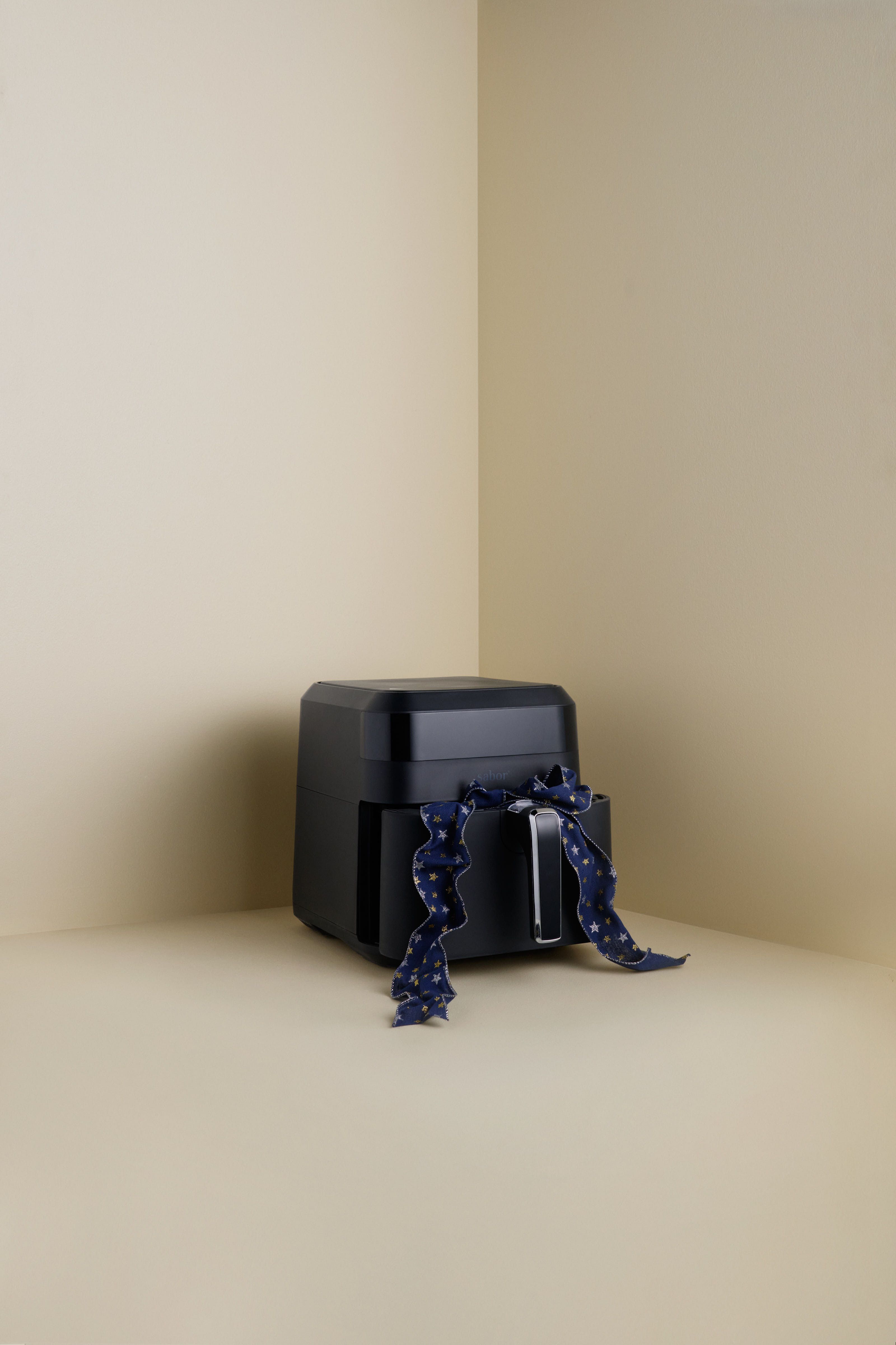 Svart airfryer med et blått bånd knyttet rundt håndtaket i et beige hjørne.