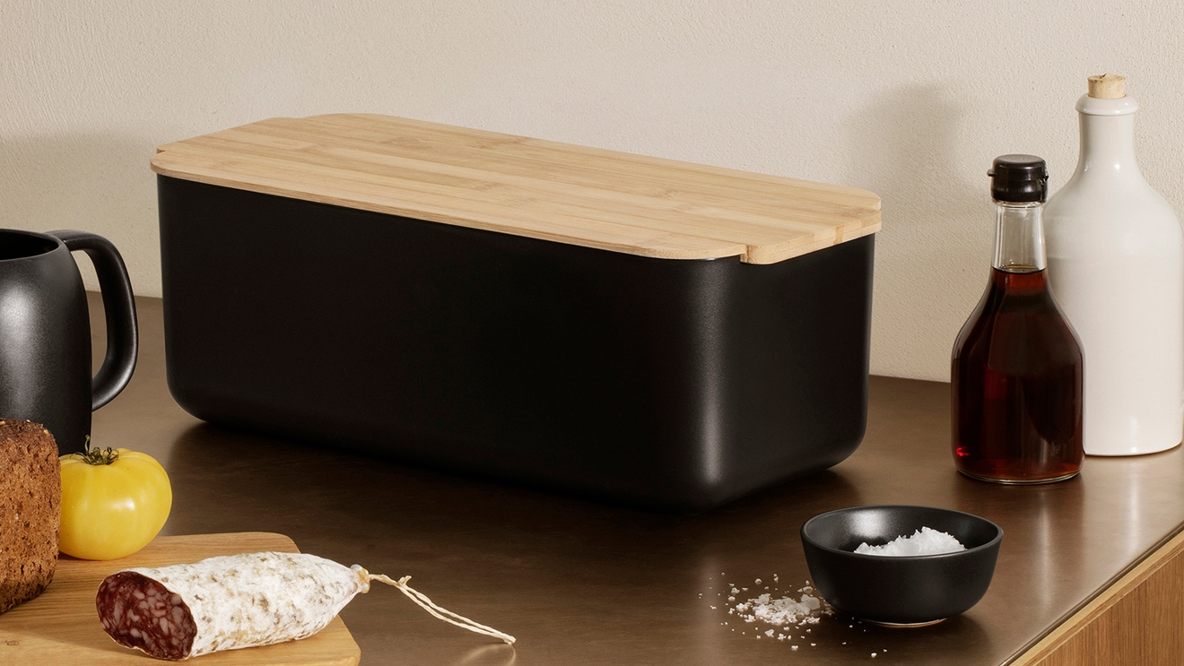 Kjøkkenoppbevaring, en svart brødboks med trelokk står på en kjøkkenbenk