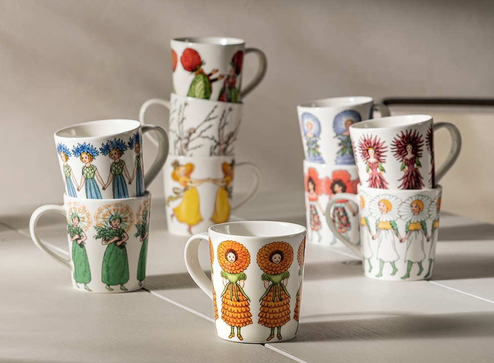 Valkoisia mukeja värikkäillä ja oikukkailla kuvioilla, osa pinottuina, vaalealla alustalla.