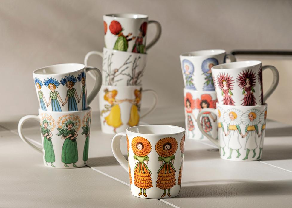 Valkoisia mukeja värikkäillä ja oikukkailla kuvioilla, osa pinottuina, vaalealla alustalla.