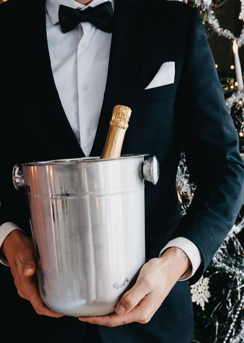 En mann i formell antrekk holder en champagnekjøler i rustfritt stål