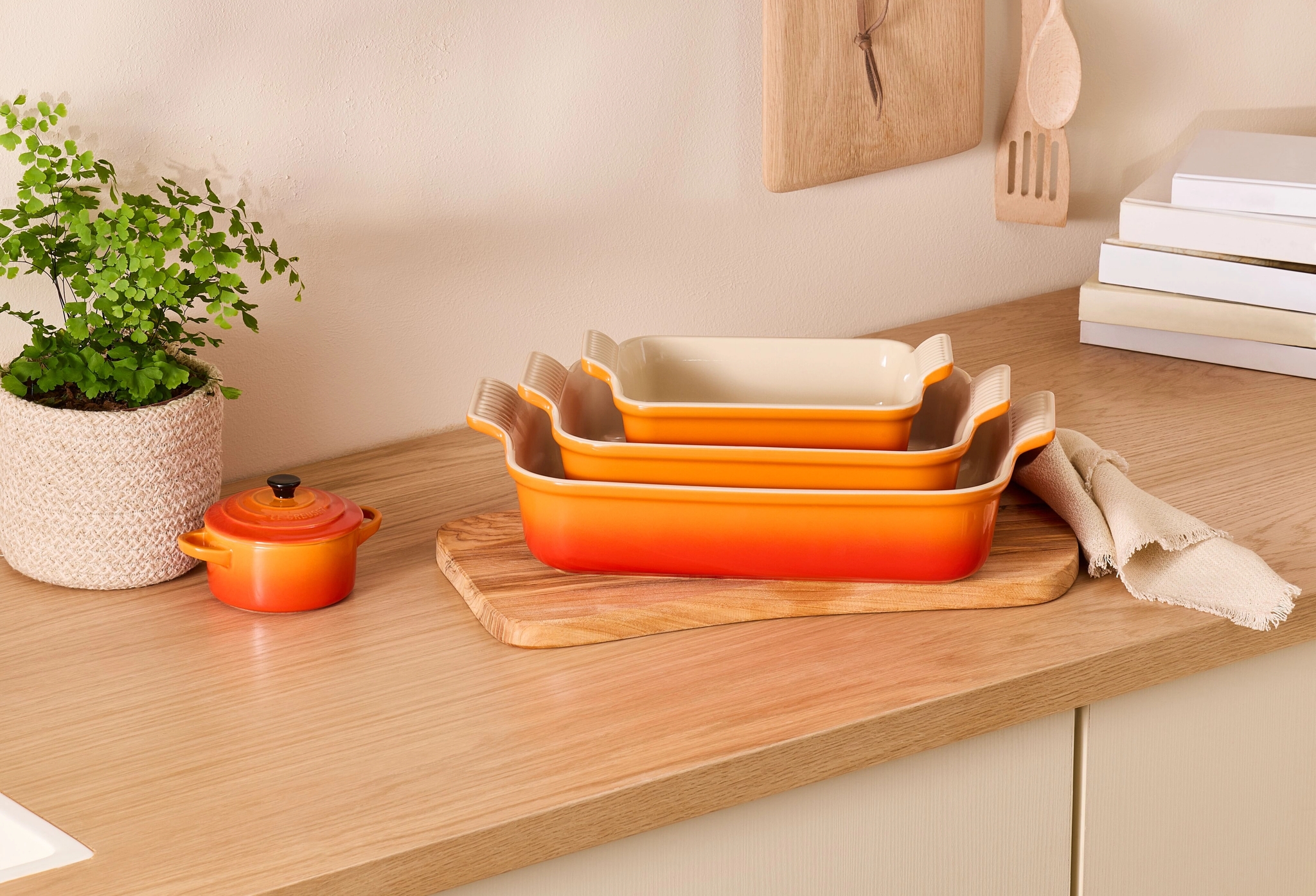 Stilren köksbänk med staplade orange ugnsformar, gröna växter och naturliga trädetaljer.