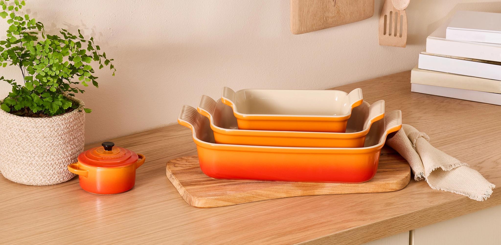 Stilren köksbänk i trä med staplade orange ugnsformar, gröna växter och kökstillbehör i naturliga material.
