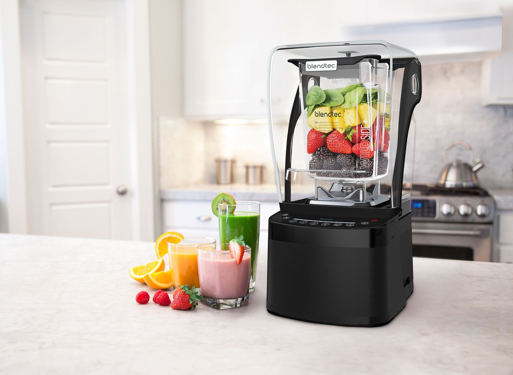 Tehokas Blendtec-tehosekoitin keittiön tasolla täynnä tuoreita hedelmiä ja marjoja, vieressä värikkäitä smoothieita laseissa.