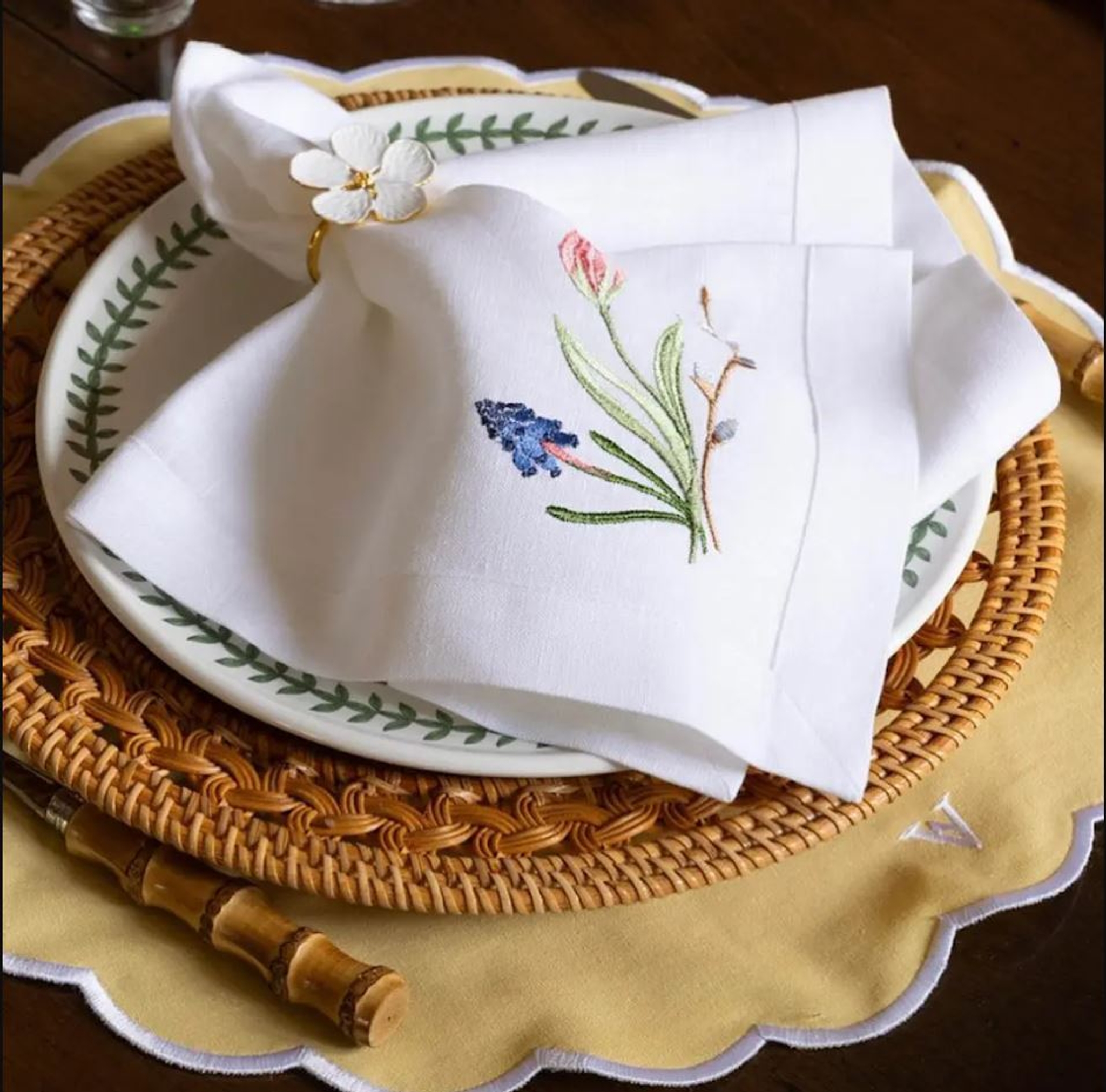 Elegant borddekking med hvit linserviett med blomsterbroderi på flettet bordbrikke og porselenstallerken