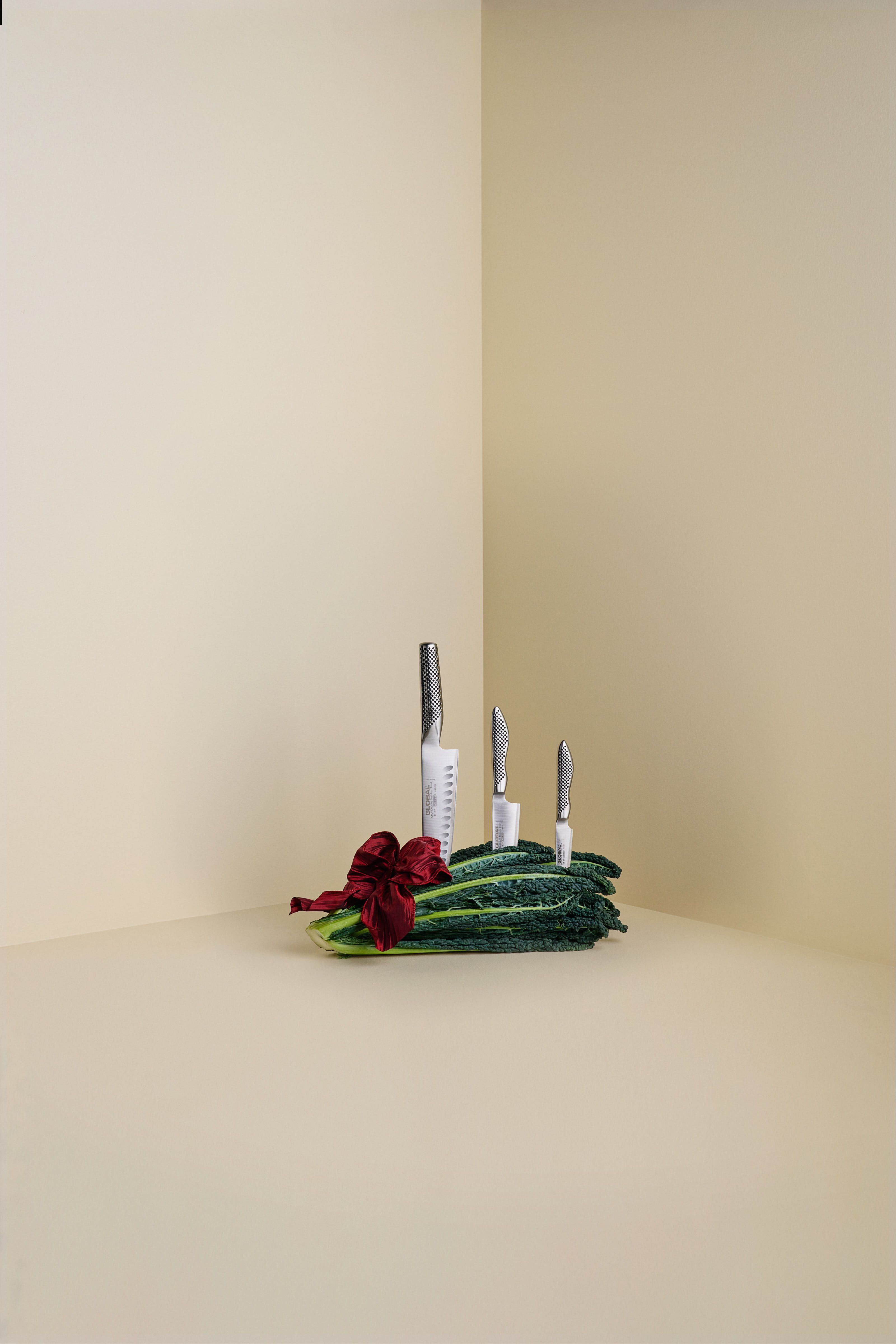 Kolme veistä pystyssä työnnettynä punaisella rusetilla sidottuun tummien lehtivihreiden nippuun beigenvärisessä nurkassa.