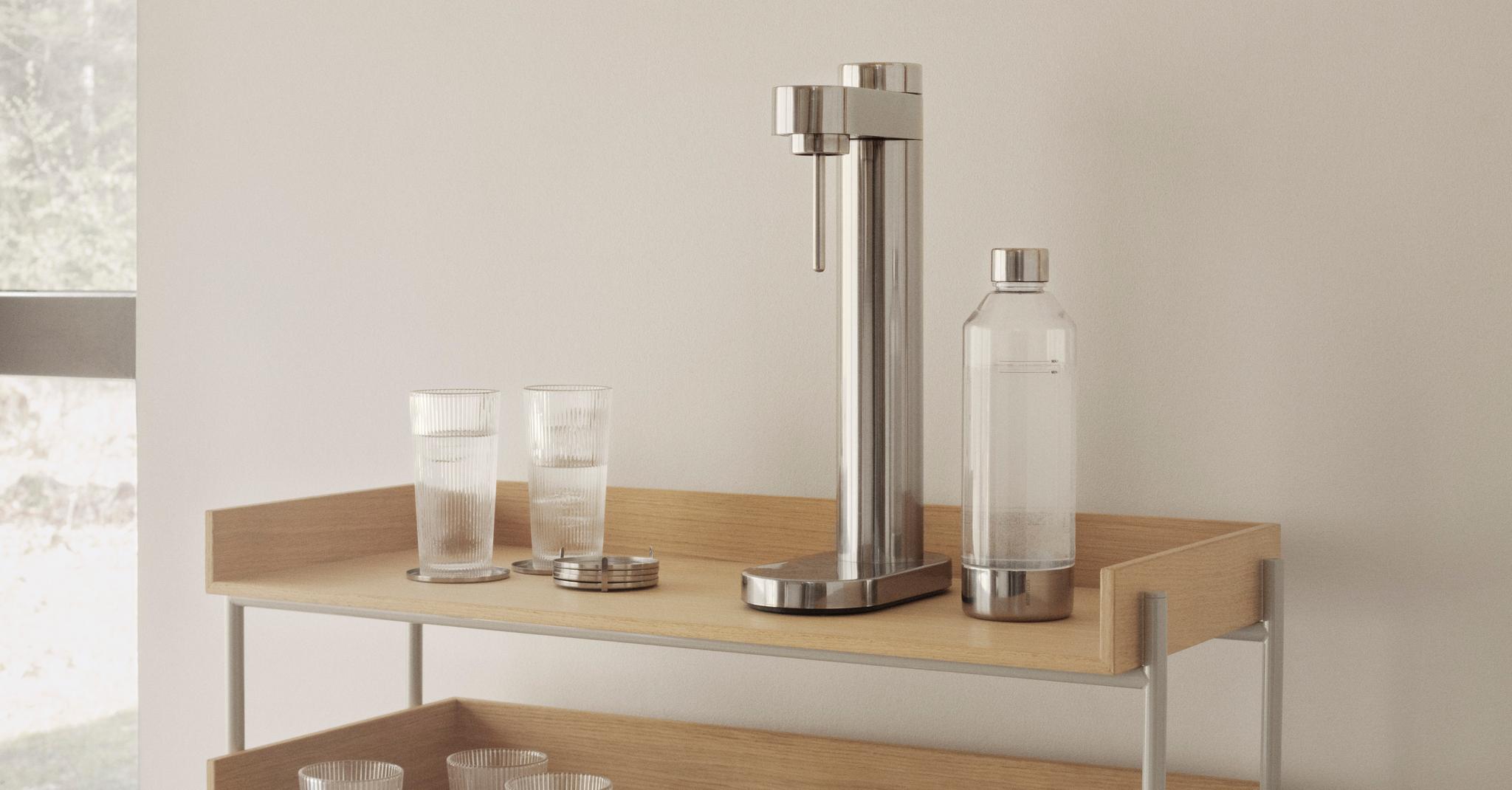 Stilren kolsyremaskin med glas och flaska på en ljus hylla i trä.
