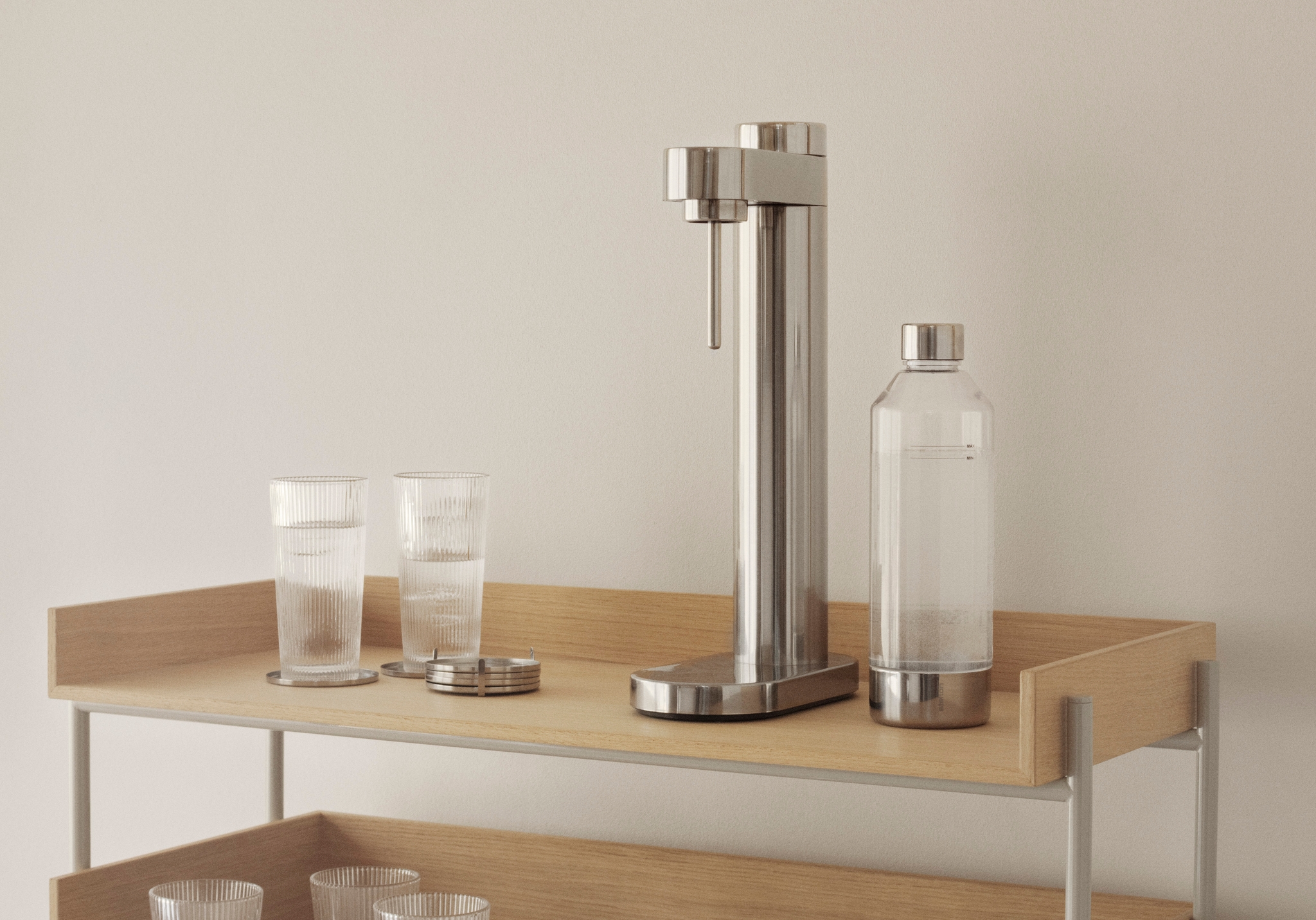 Minimalistisk köksbänk i ljust trä med kolsyremaskin, glas och stilrena köksdetaljer i ett modernt skandinaviskt hem.