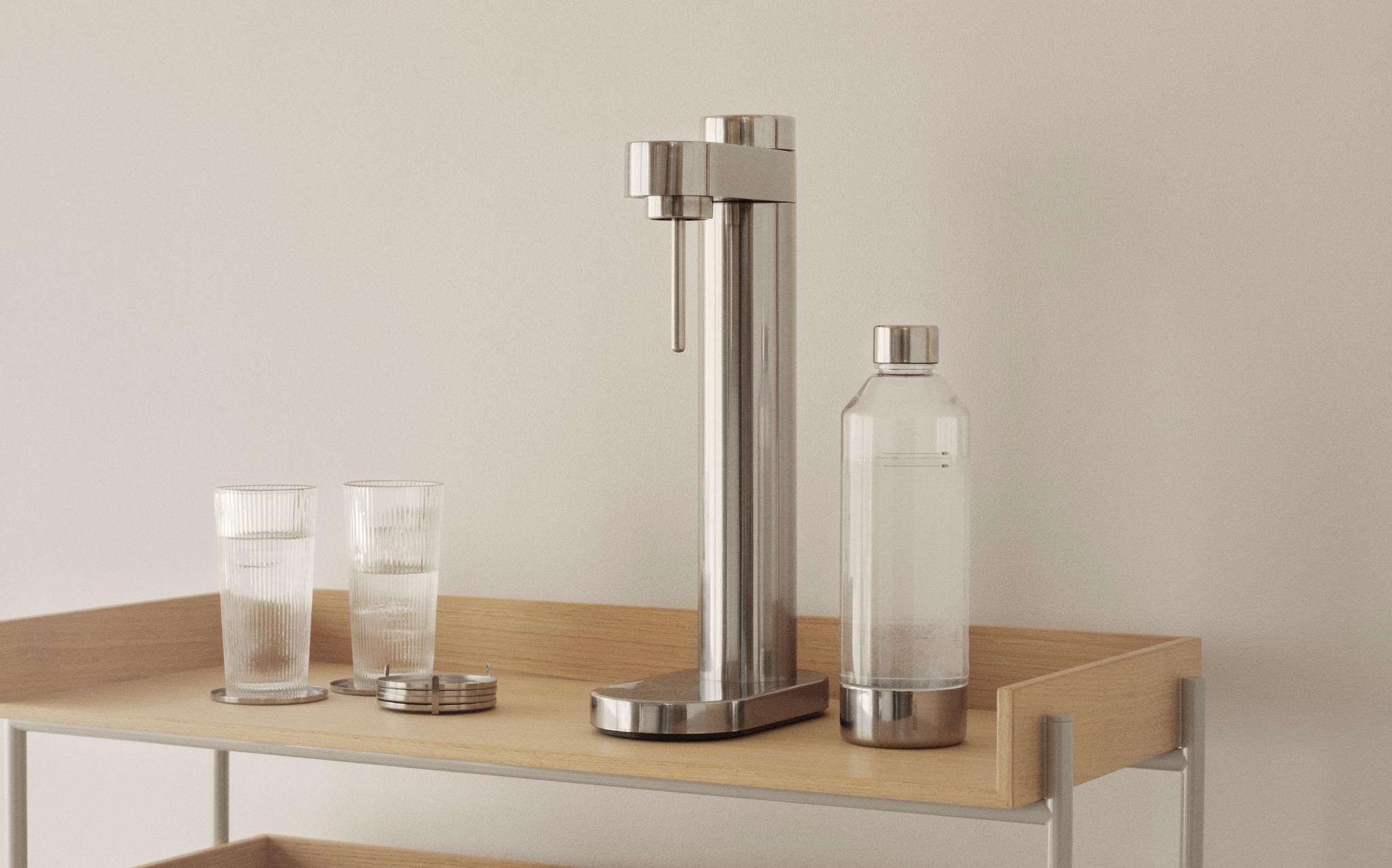 Vaaleapuinen hyllykkö, jonka sisustukseen kuuluu uurrettuja laseja, jääämpäri, kirjoja, limsakone ja puisia myllyjä.