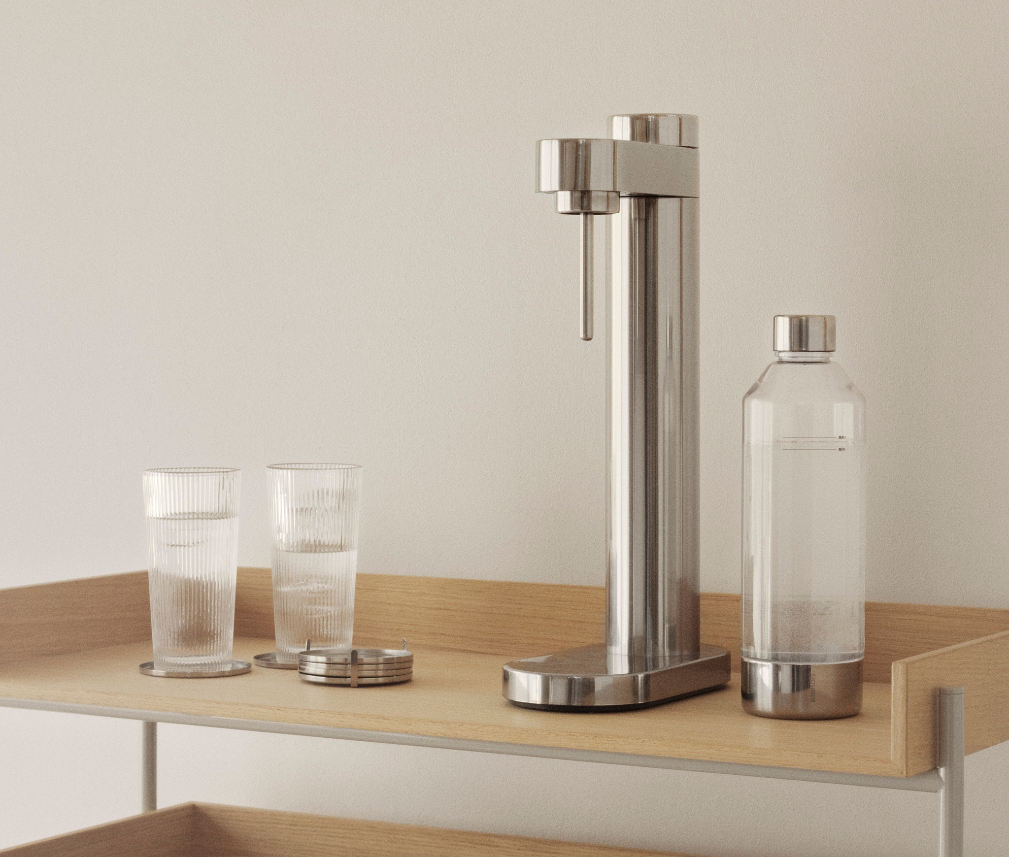 Vaaleapuinen hyllykkö, jonka sisustukseen kuuluu uurrettuja laseja, jääämpäri, kirjoja, limsakone ja puisia myllyjä.