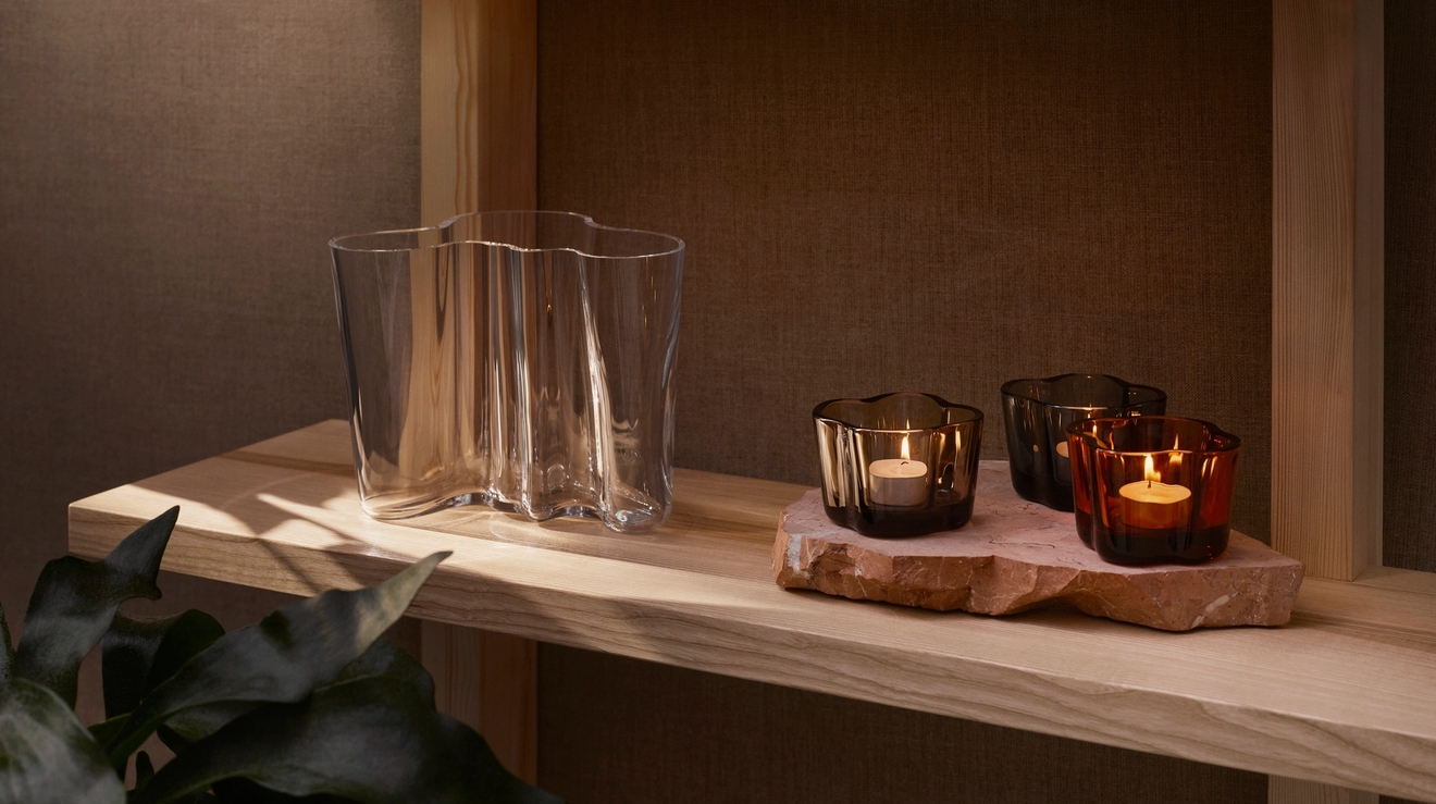 Tre ljusstakar står på en trähylla bredvid en Alvar Aalto-vas.