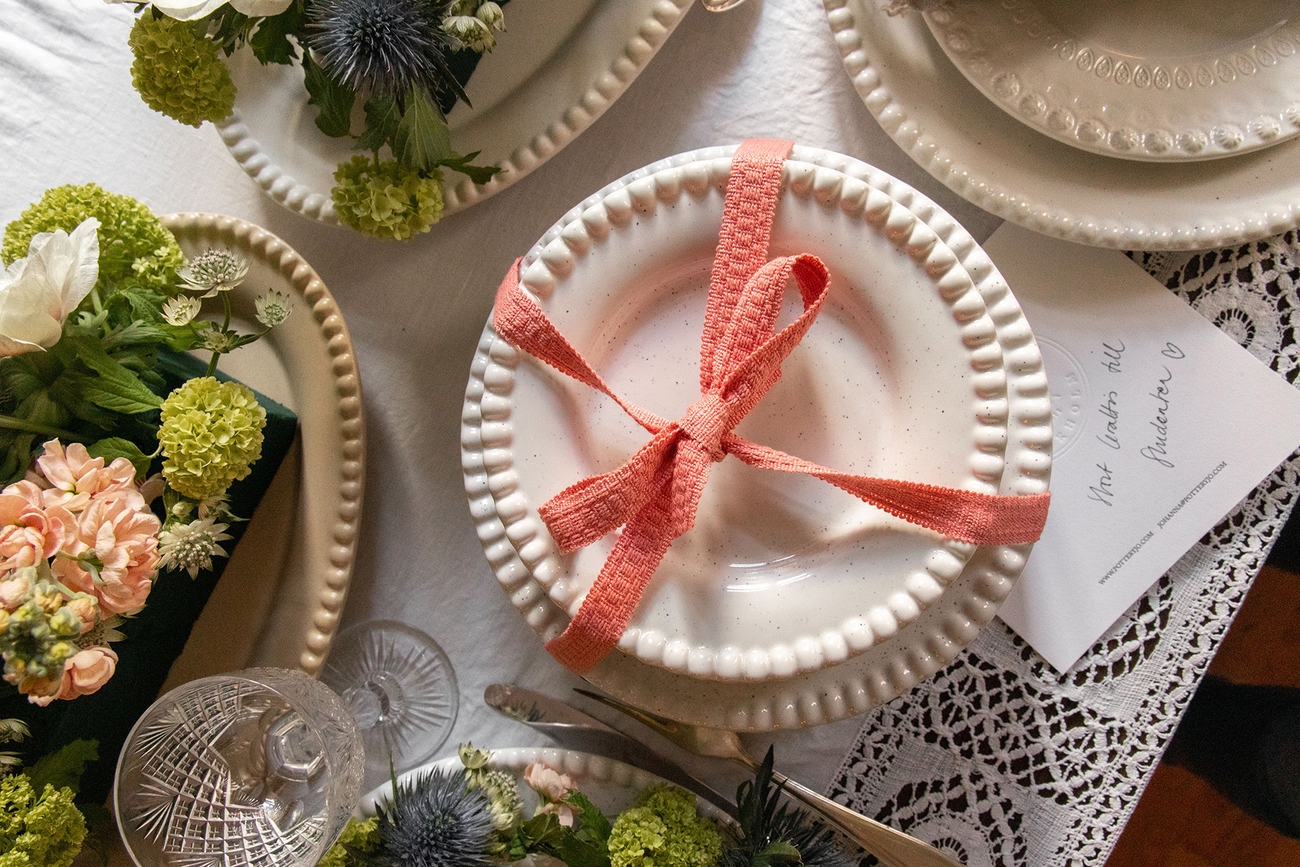 Ett gratulationskort under ett paket med tallrikar inslagna med ett snöre och blommor