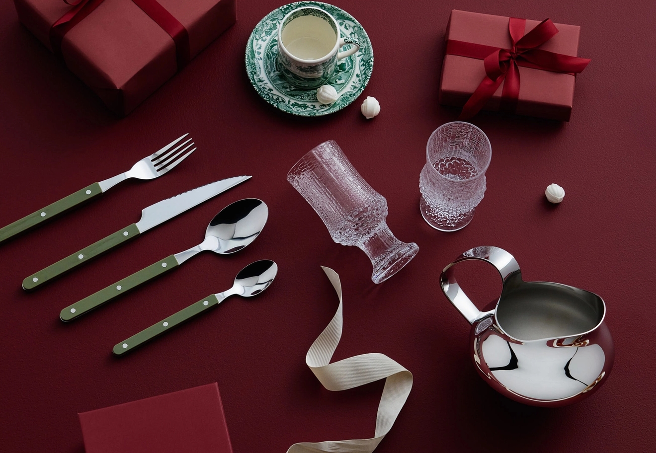 Två röda presentaskar, bestick med grönt handtag, en tekopp, glasmuggar och en silverkanna mot röd bakgrund.