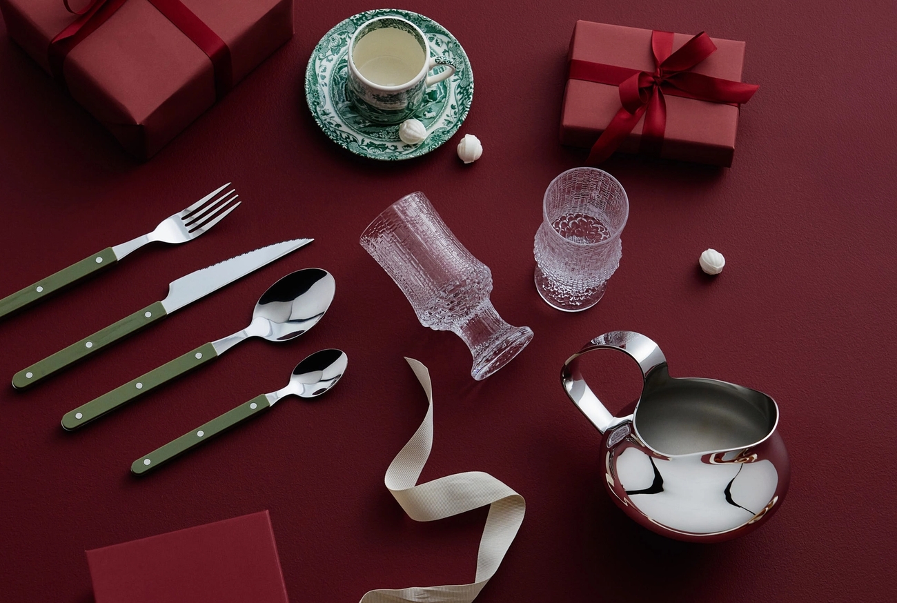 Två röda presentaskar, bestick med grönt handtag, en tekopp, glasmuggar och en silverkanna mot röd bakgrund.