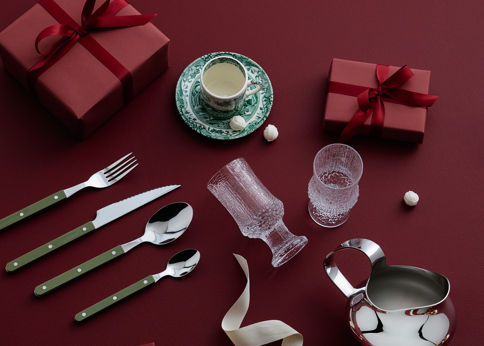Röda presentaskar, bestick med gröna handtag, en tekopp och glas arrangerade på en mörkröd yta.