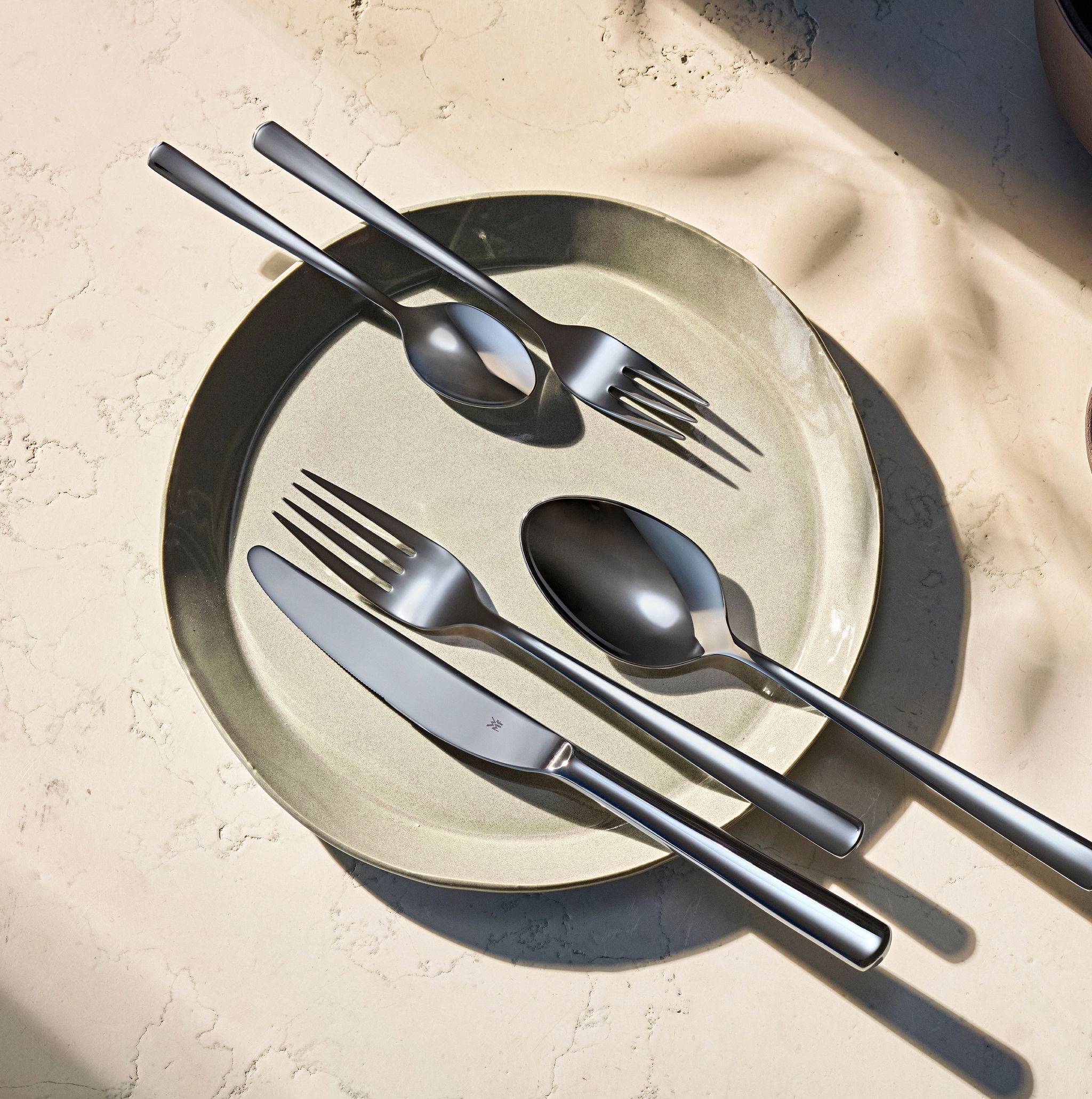 Moderneja aterimia vaaleanvihreällä lautasella, pieni kulho pähkinöitä ja voimakkaita varjoja.