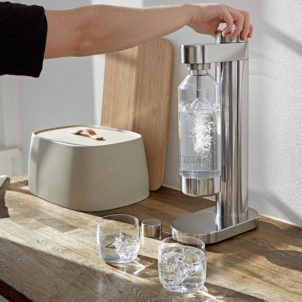 En person gör kolsyrat vatten i en kolsyremaskin i stål från Stelton Brus