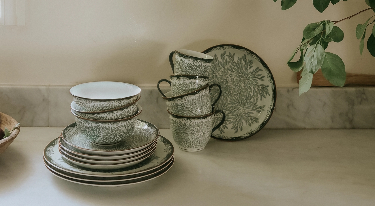 Porslin från Rörstrand Ostindia Floris grön står staplade på en köksbänk