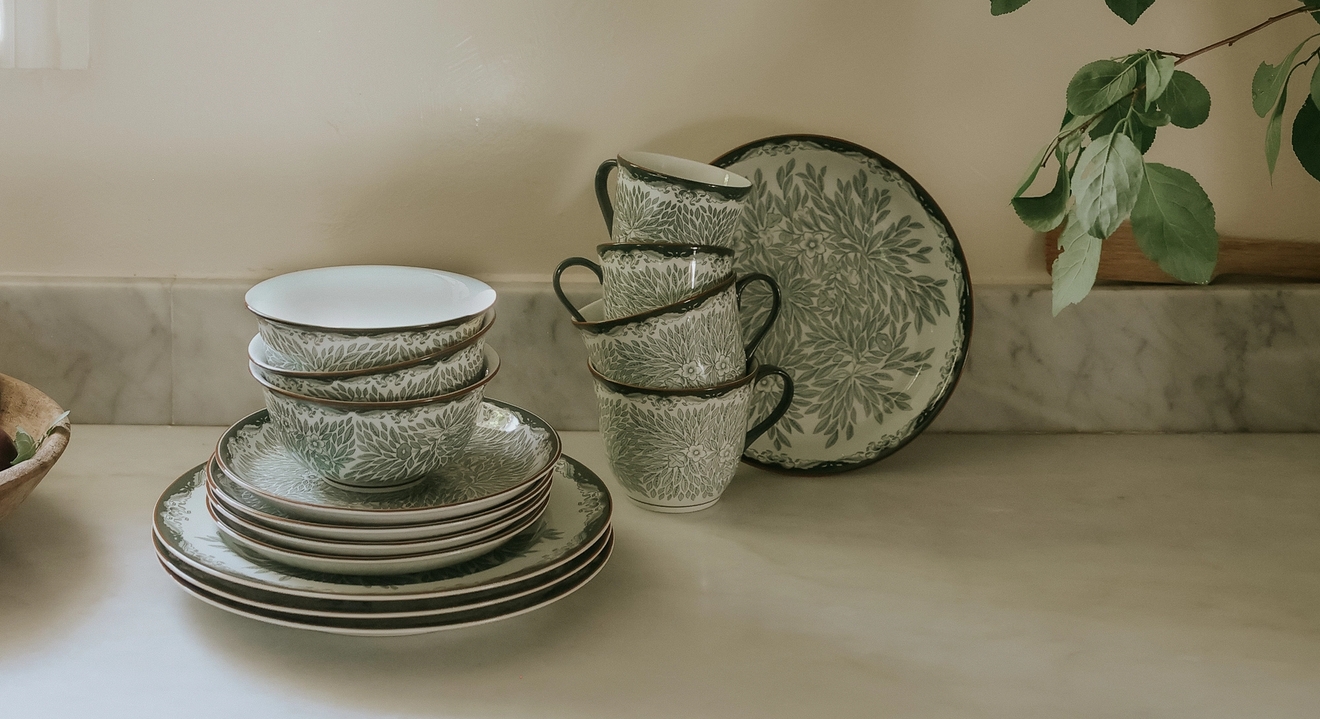 Porslin från Rörstrand Ostindia Floris grön står staplade på en köksbänk