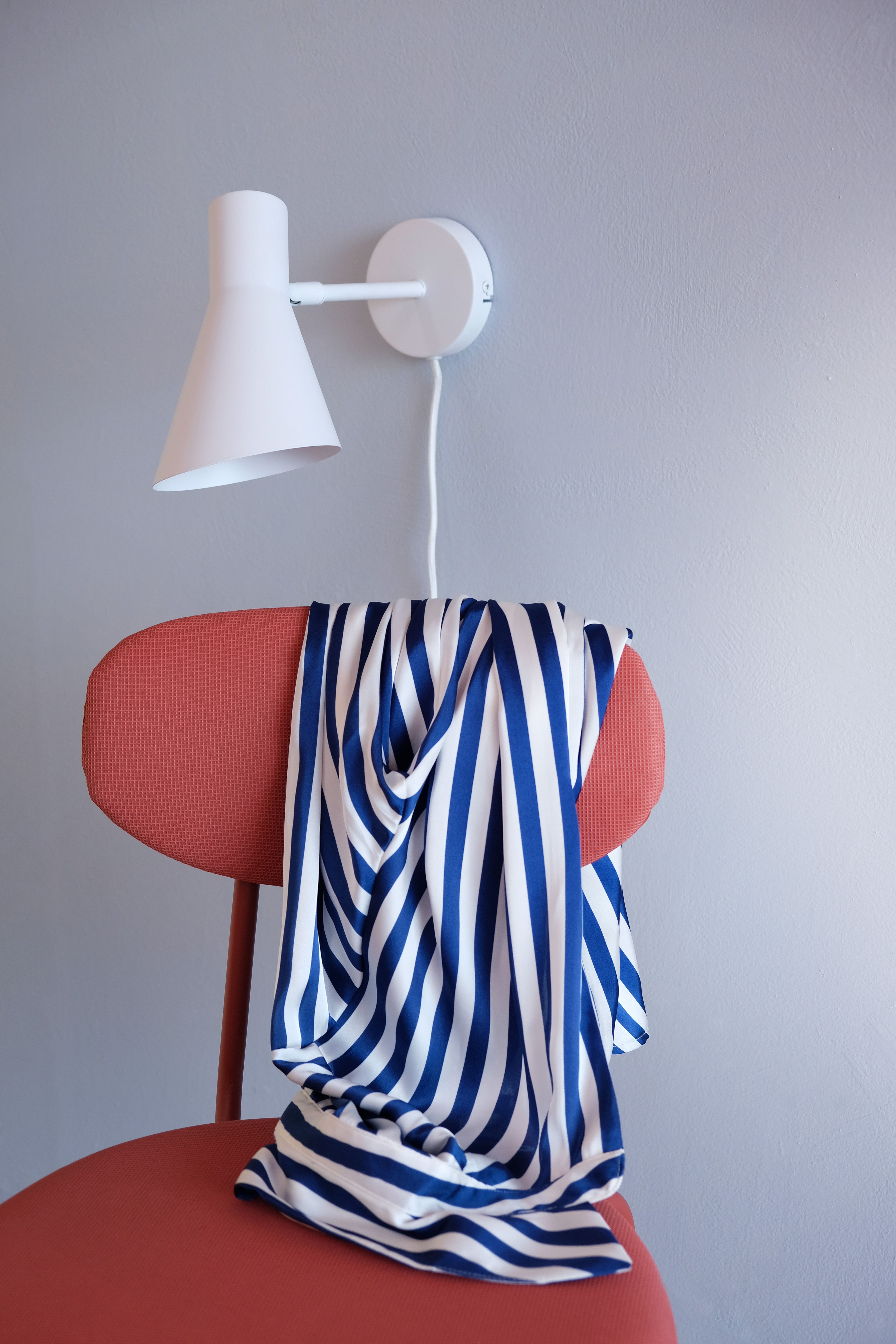 Blåvitrandigt tyg draperat över en röd stol under en vit vägglampa.