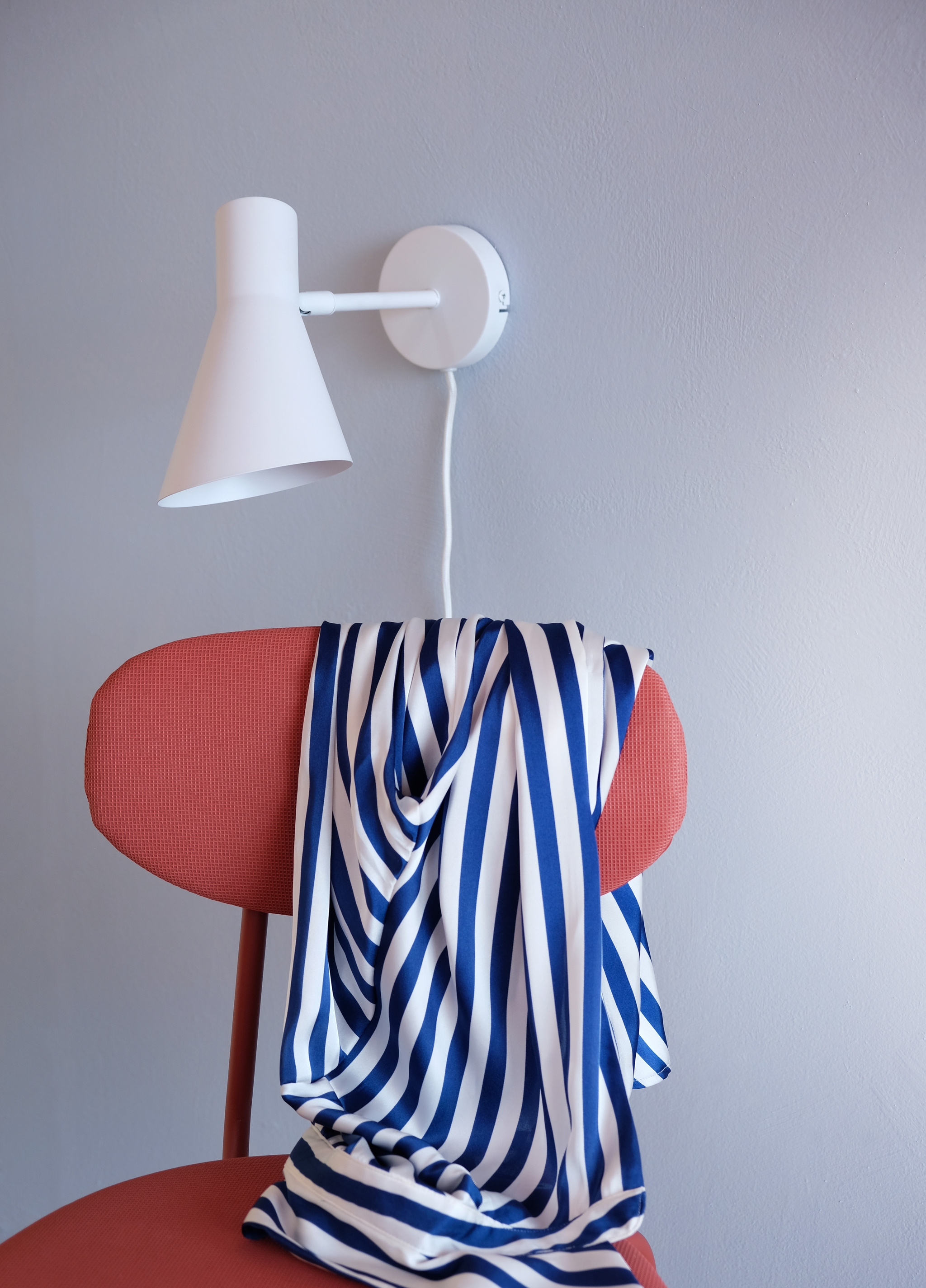 Blåvitrandigt tyg draperat över en röd stol under en vit vägglampa.