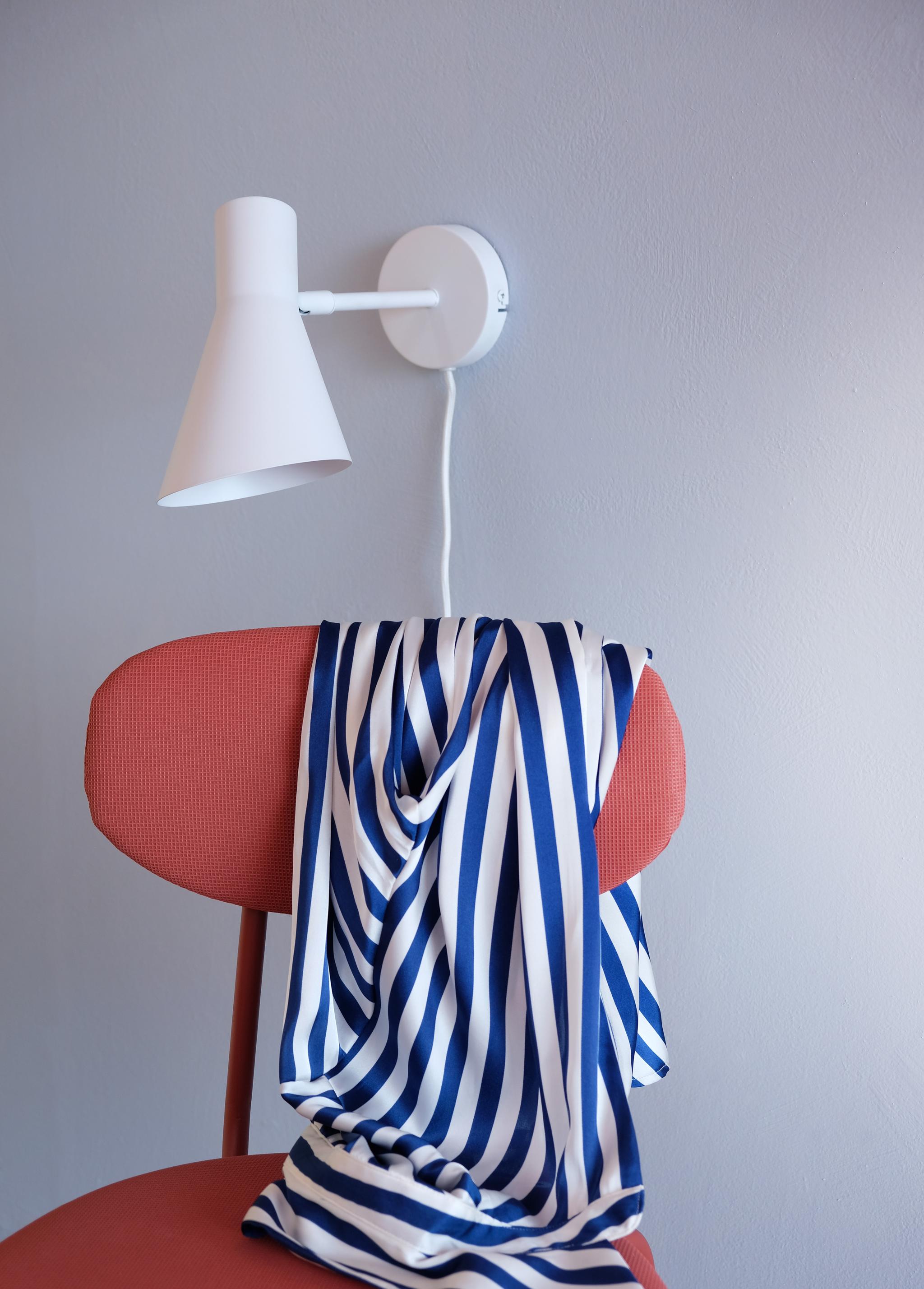Blåvitrandigt tyg draperat över en röd stol under en vit vägglampa.