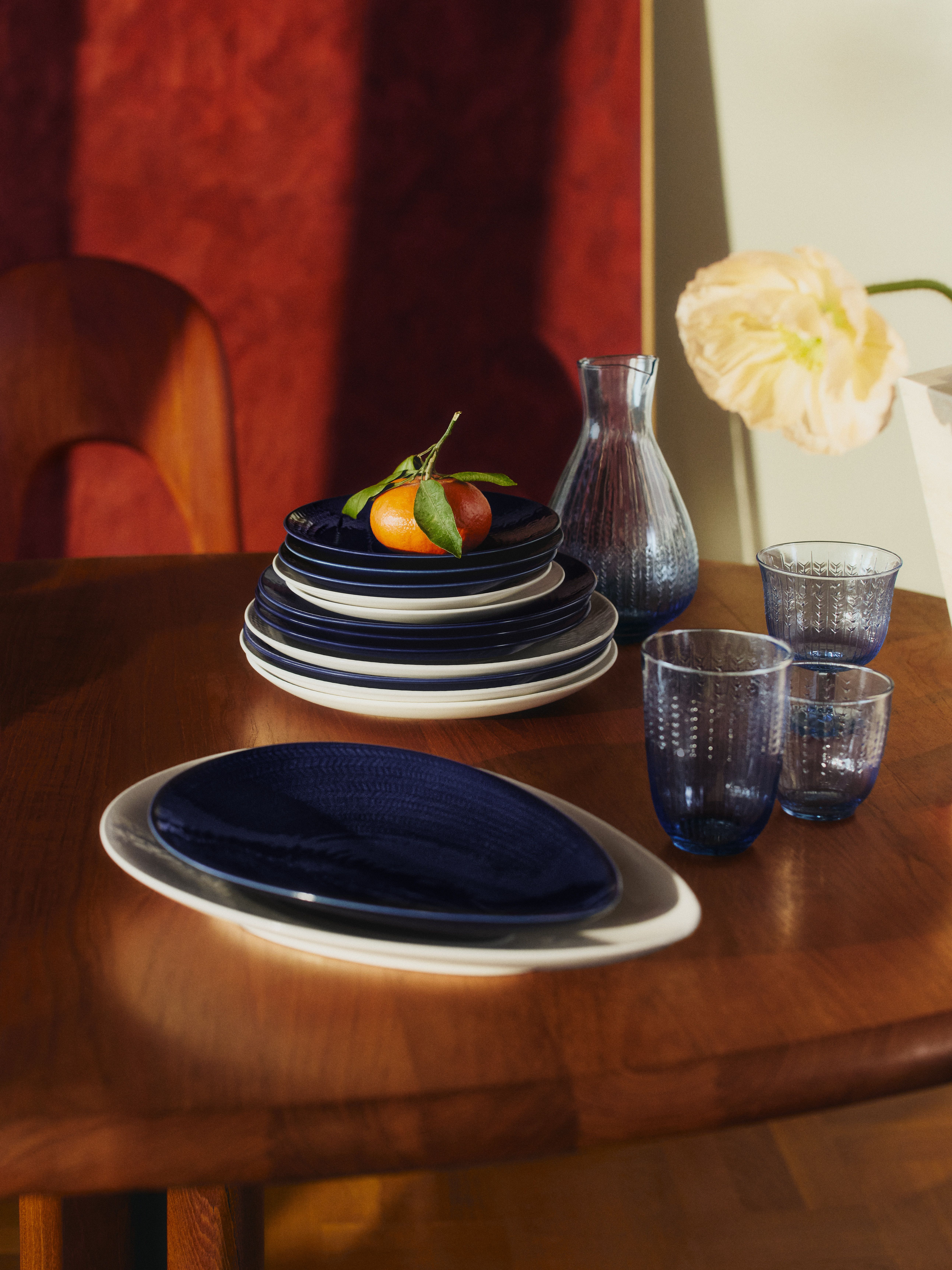 Dukat träbord med blått porslin, glas och en mandarin som dekoration i varmt solljus.