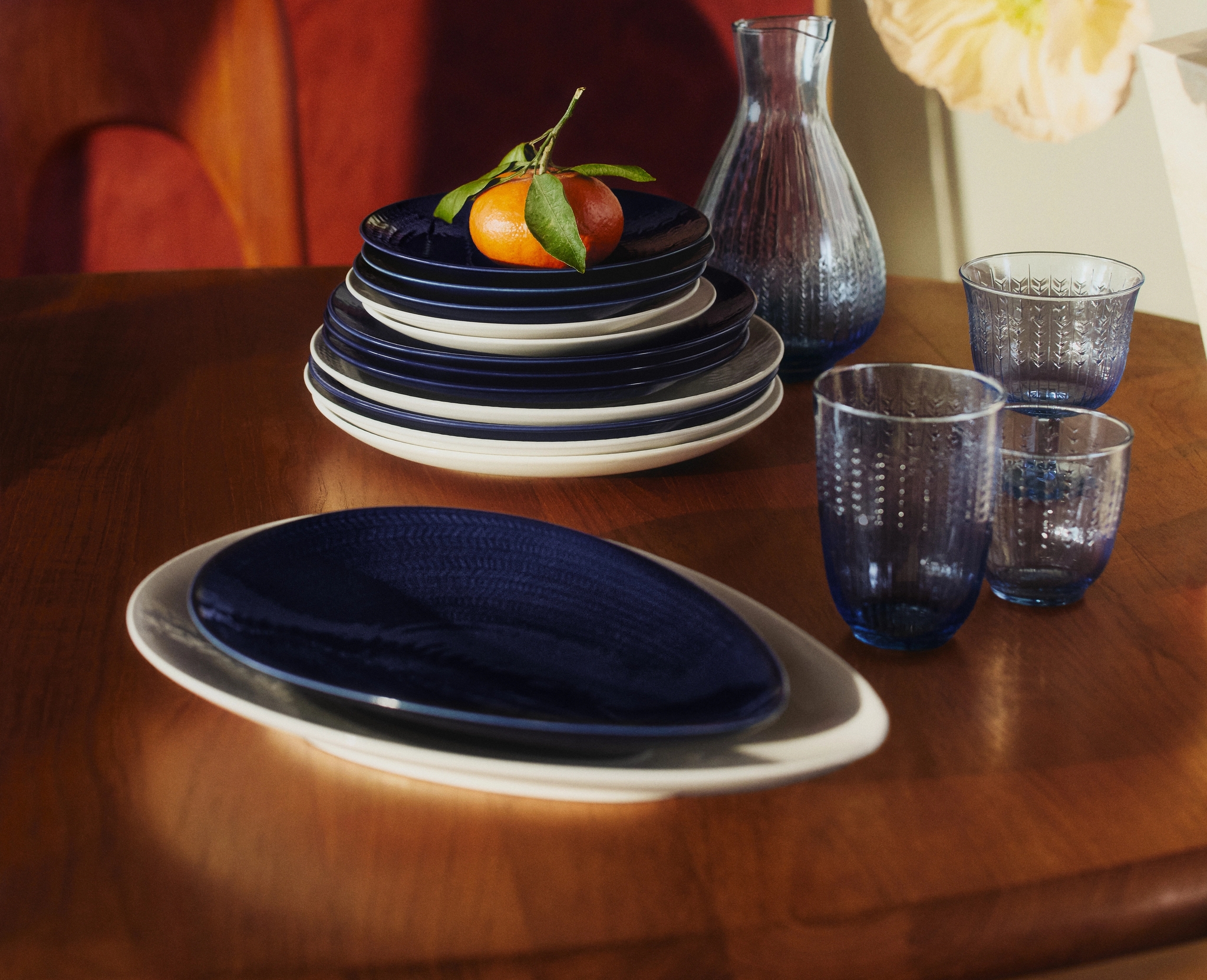 Dukat träbord med blått porslin, glas och en mandarin som dekoration i varmt solljus.