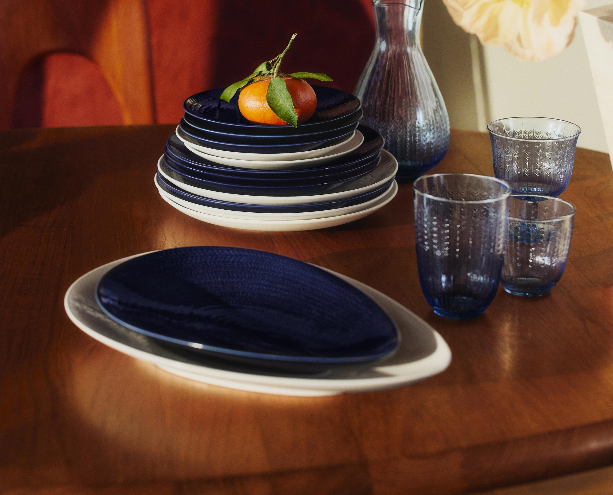 Dukat träbord med blått porslin, glas och en mandarin som dekoration i varmt solljus.