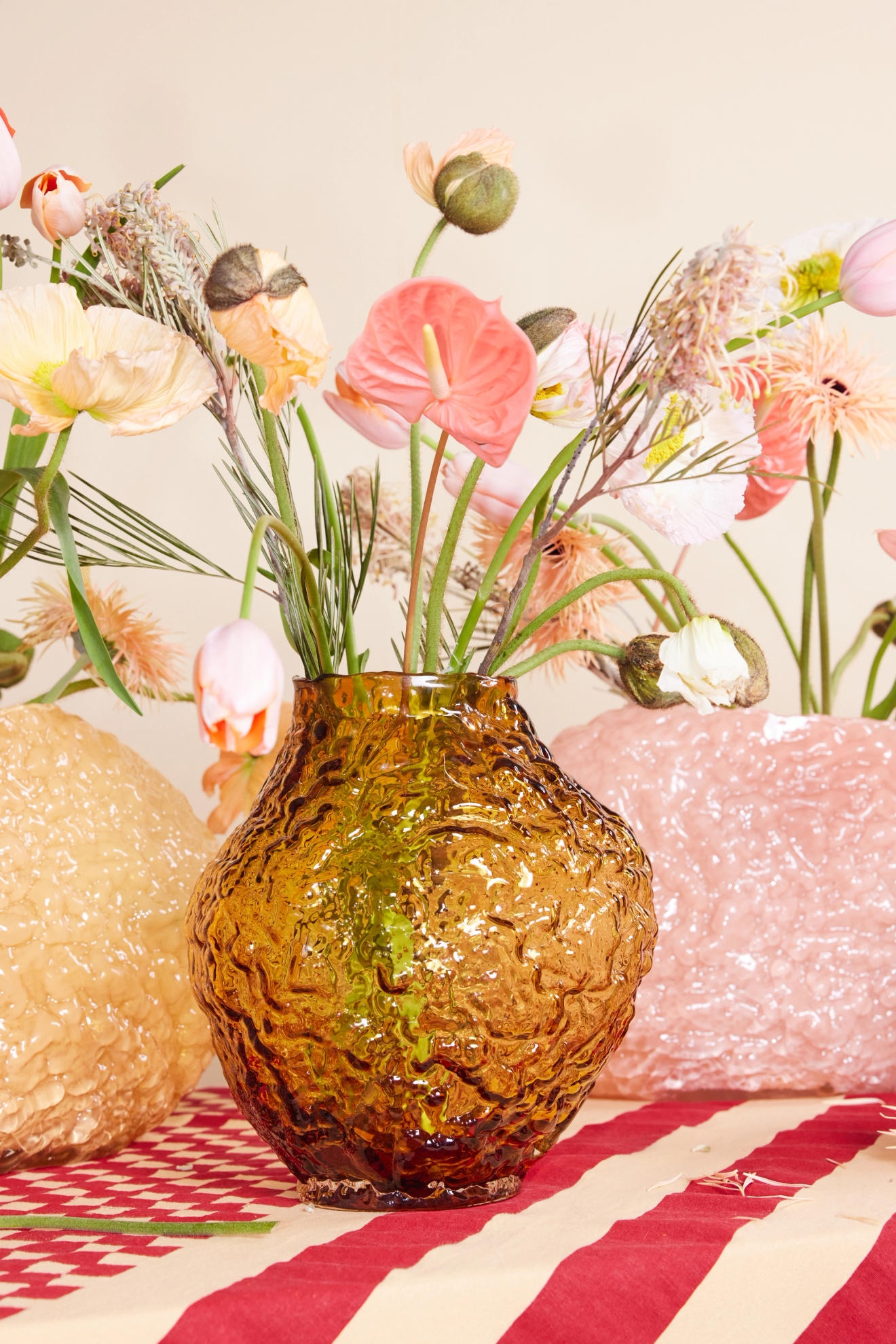ByOn vas i gulfärgat glas med struktur, placerad på en röd vit randig duk omgiven med andra vaser och blommor