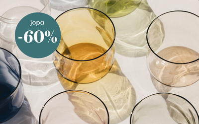 Värikkäät juomalasit aseteltuna pöydälle ja vihreä merkki, jossa lukee jopa -60 % alennus.
