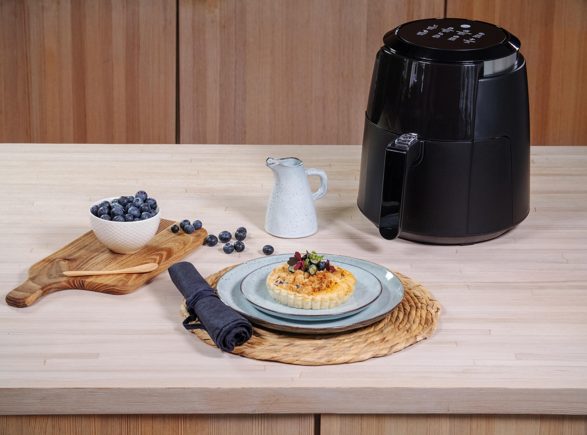 Pieni airfryer keittiön työtasolla ja makea piirakka vaaleansinisellä lautasella mustikoiden kera