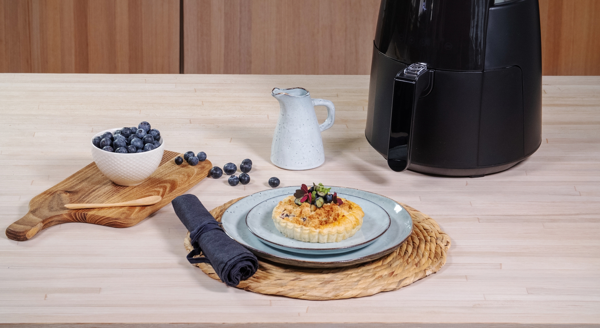 Pieni airfryer keittiön työtasolla ja makea piirakka vaaleansinisellä lautasella mustikoiden kera