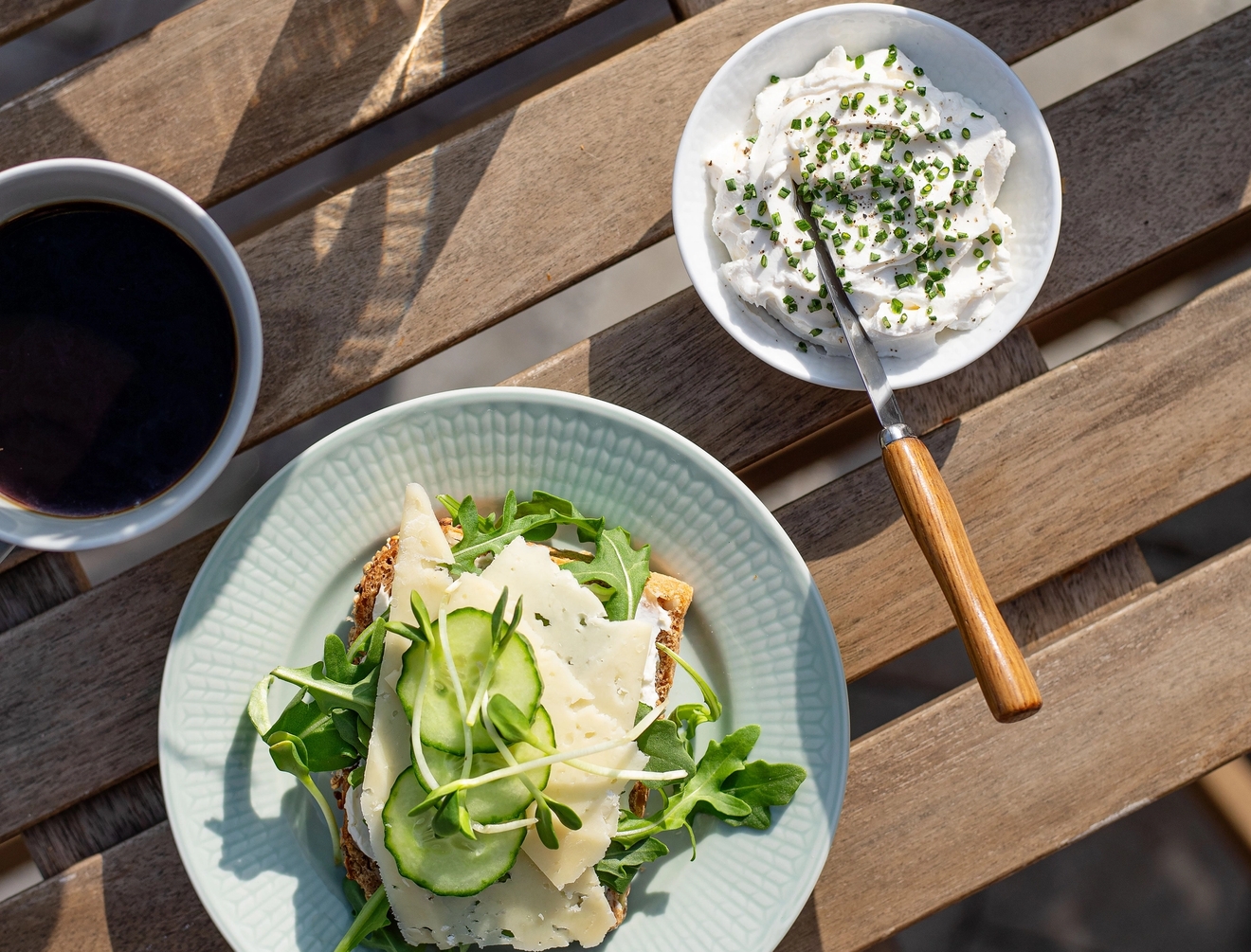 God smörgås på en tallrik och en kopp kaffe på ett träbord utomhus