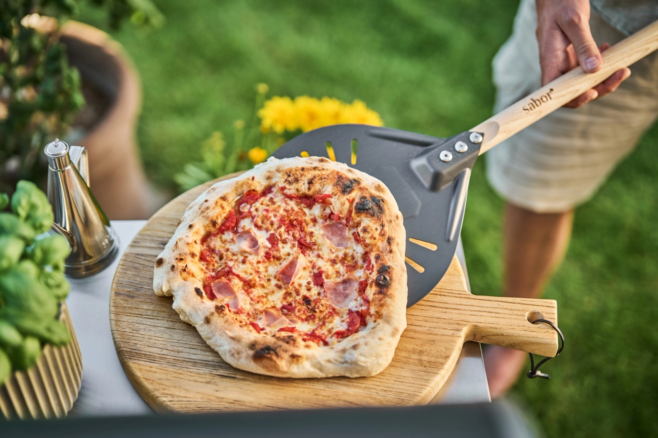 Puulapiolla nostettava vastapaistettu pizza ulkokeittiössä puutarhassa.