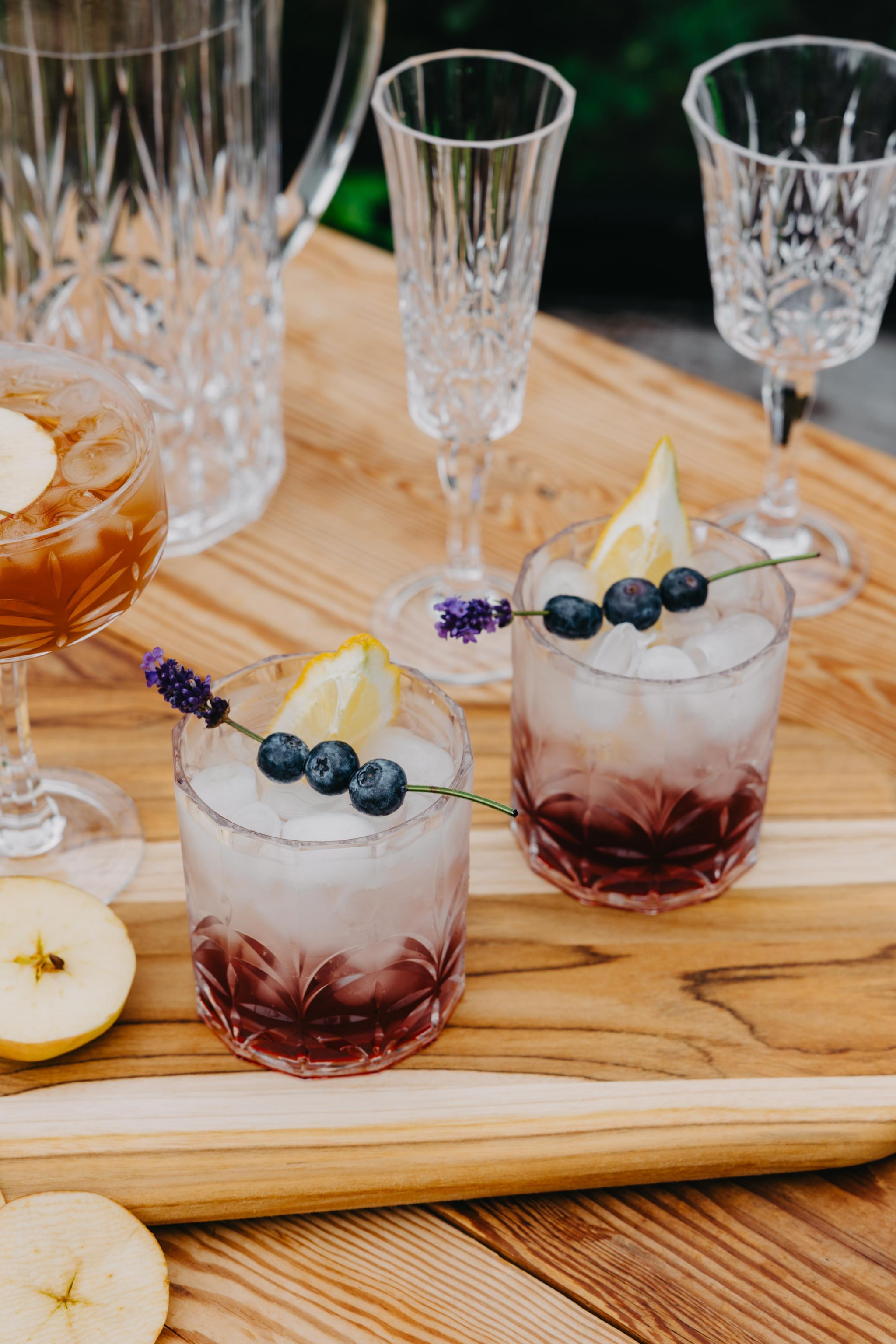 Somrig drink med blåbär, citron och is serverad i kristallglas på en träbricka.
