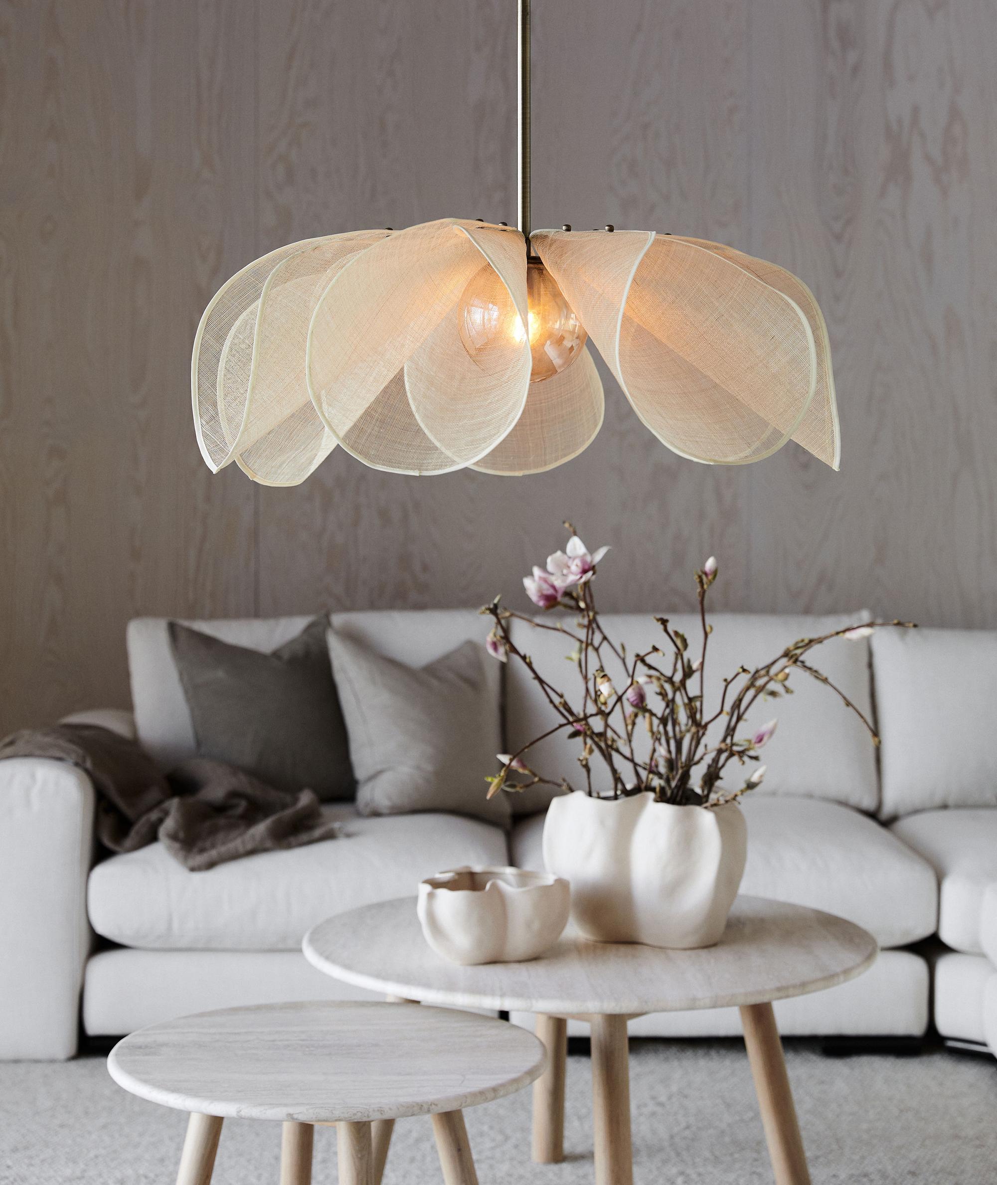 En blomformad pendellampa med genomskinliga tygblad hänger ovanför ett soffbord och en vit soffa.