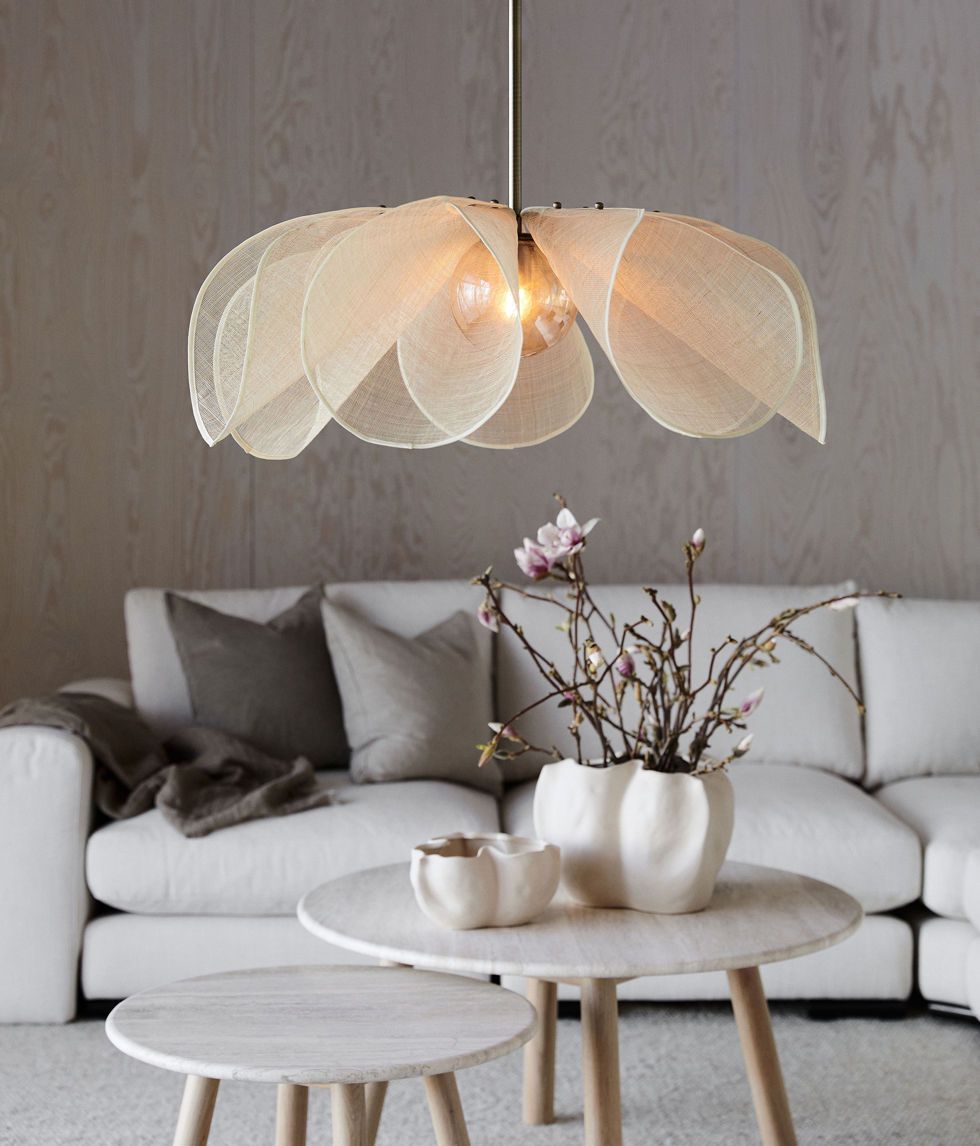 En blomformad pendellampa med genomskinliga tygblad hänger ovanför ett soffbord och en vit soffa.