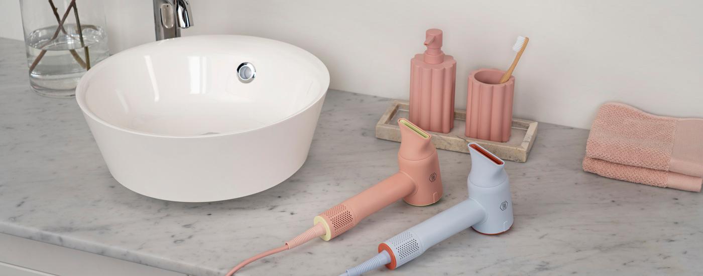 Stilrent badrum med handfat, rosa detaljer och två elektriska tandborstar på en marmorbänk.