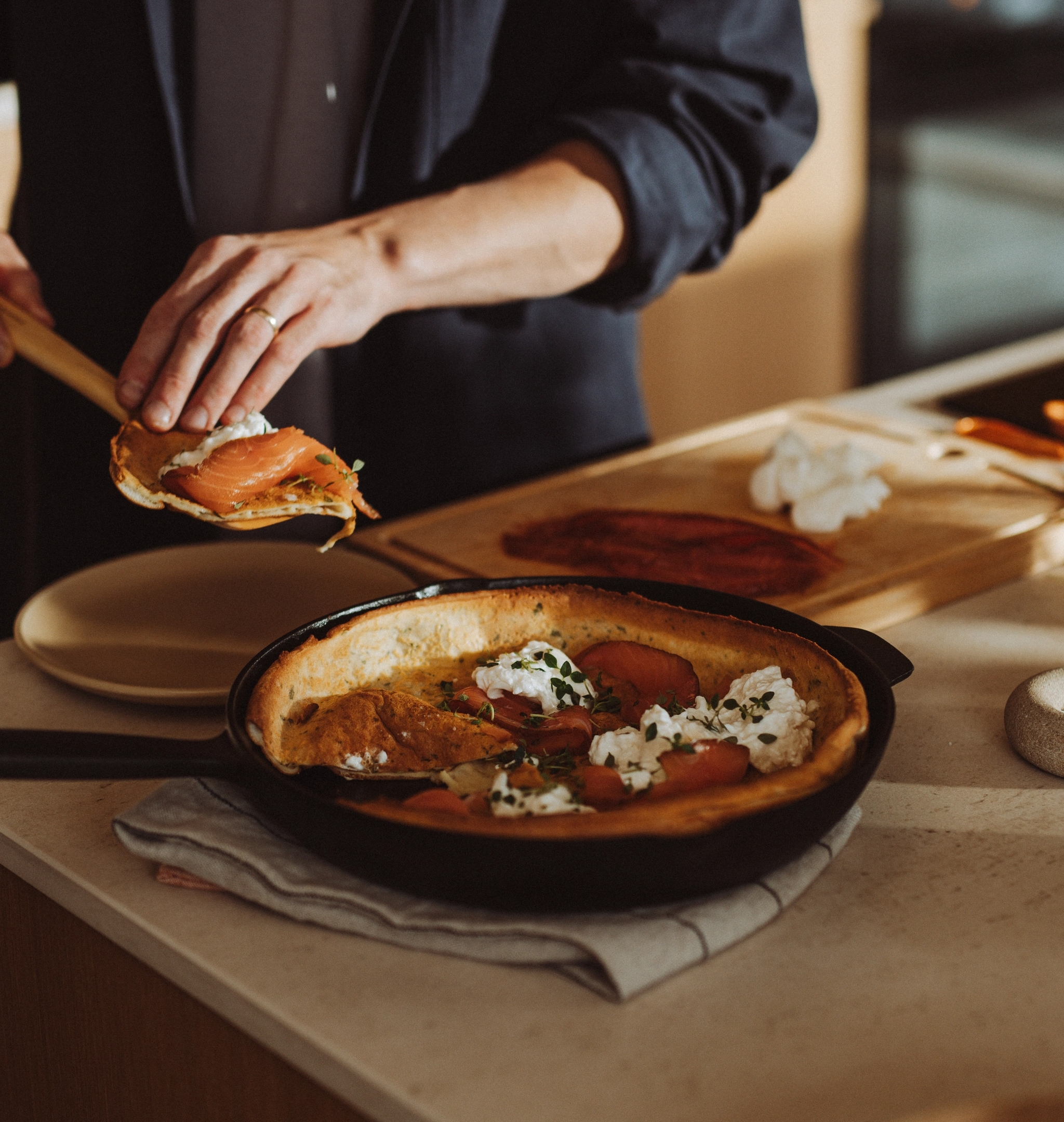 En person garnerar en holländsk pannkaka med lax och ost i ett kök.
