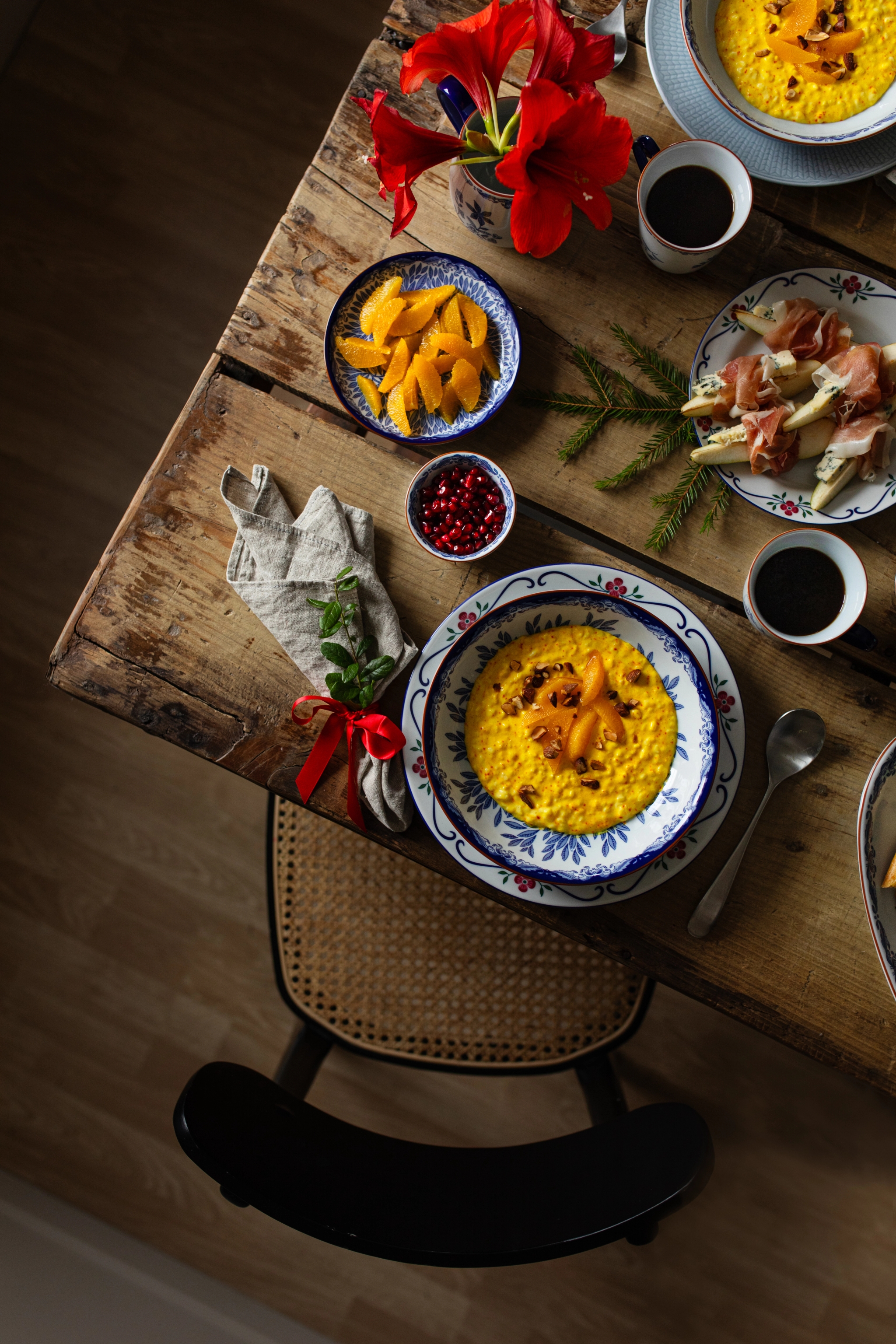 Juldukning på rustikt träbord med saffransgröt, apelsin, granatäpple, kaffe, skinka och röda amaryllis.