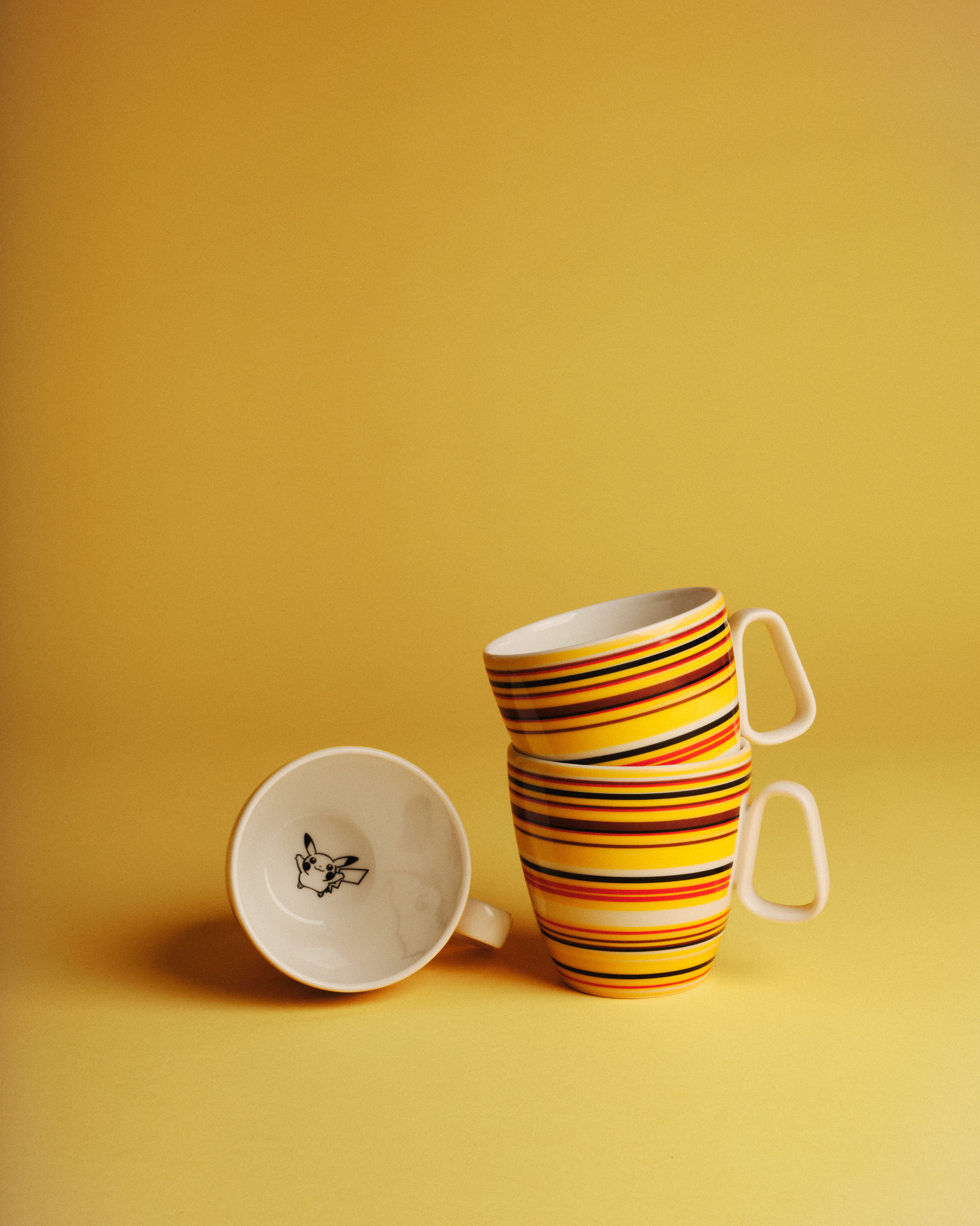 Tre färgglada randiga kaffekoppar står mot en gul bakgrund, varav en visar en tecknad figur inuti.