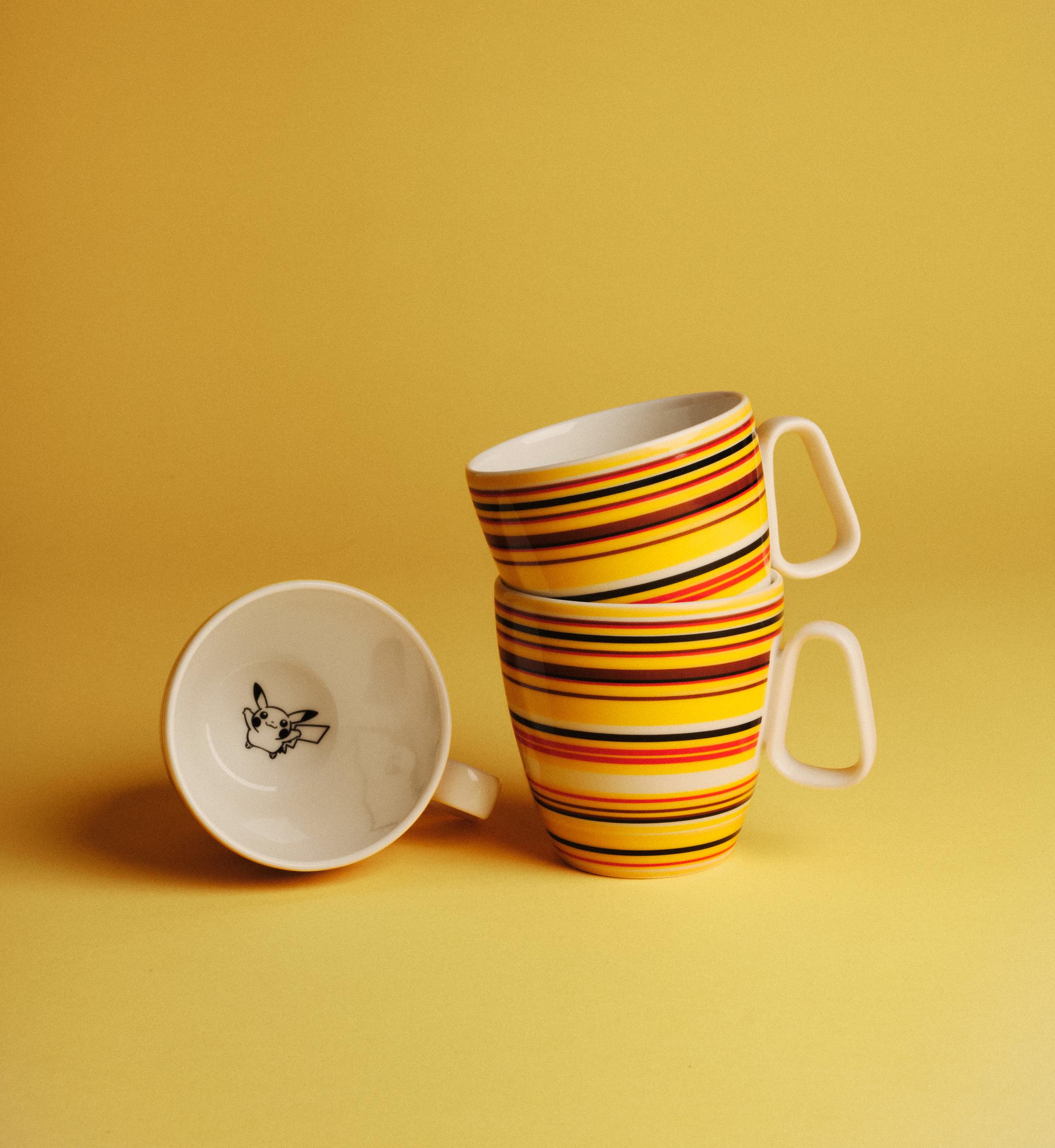 Tre färgglada randiga kaffekoppar står mot en gul bakgrund, varav en visar en tecknad figur inuti.