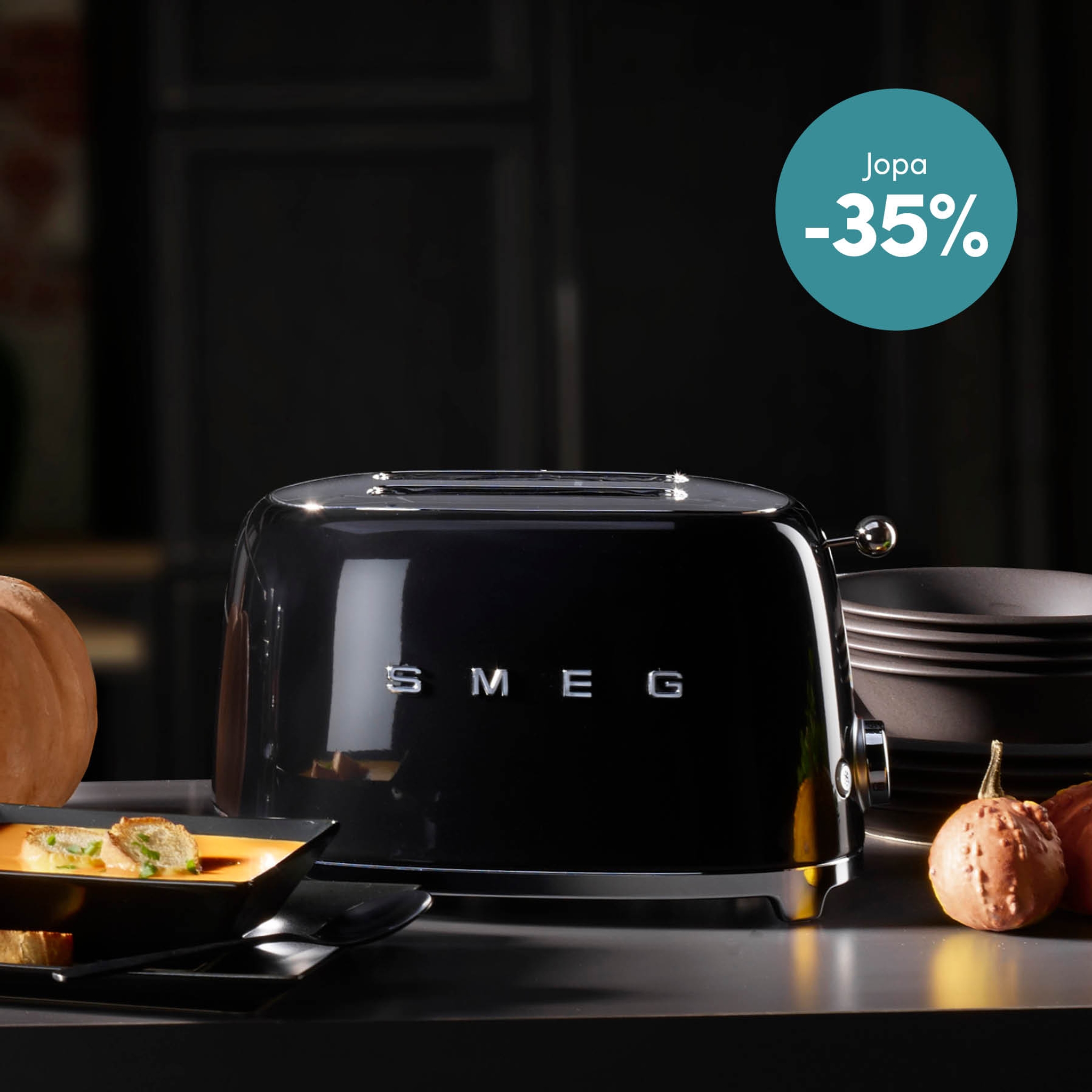 Musta Smeg-leivänpaahdin tummalla tiskillä, kulho keittoa ja kurpitsoja.