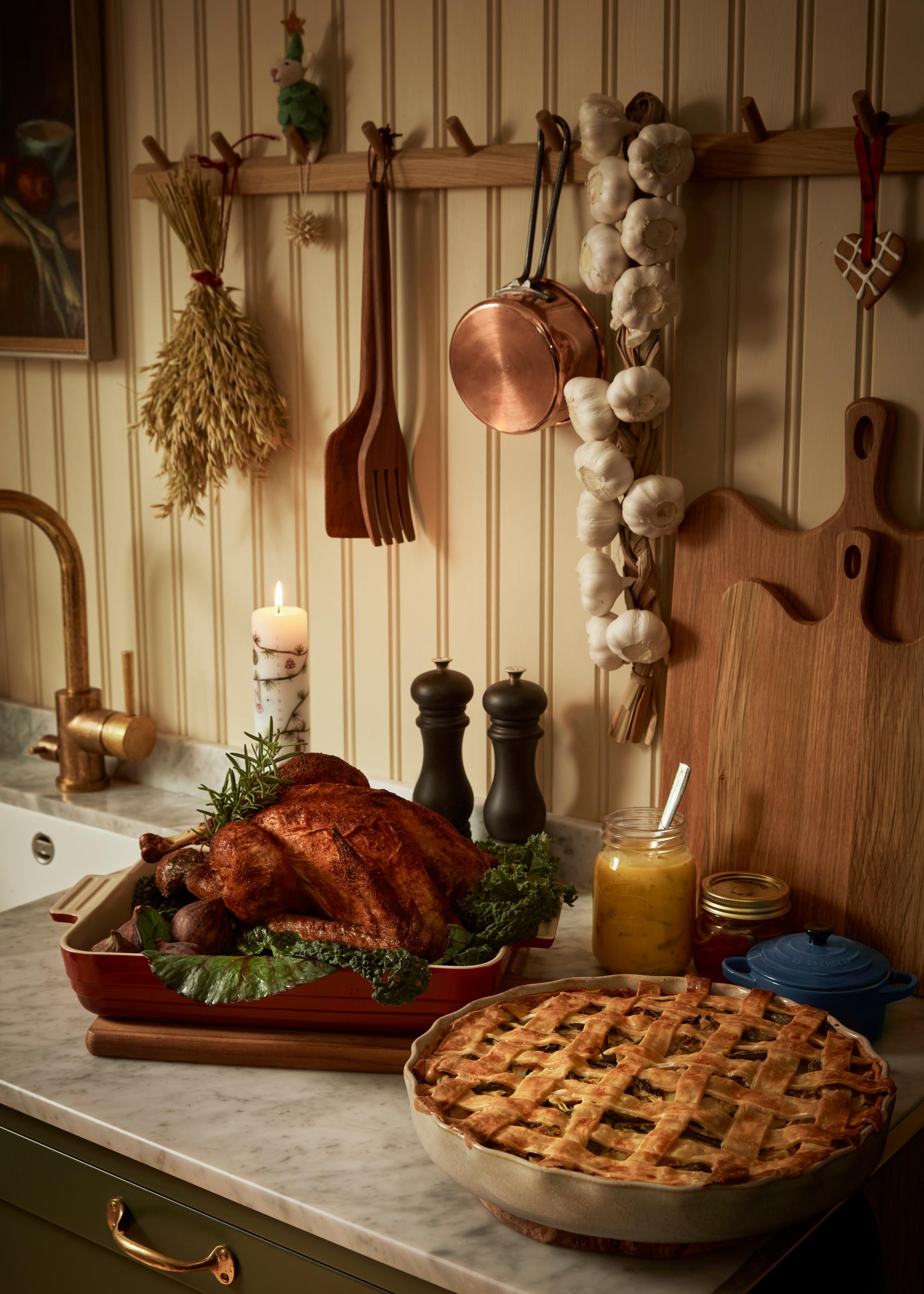 Kullanruskeaksi paistettu kalkkipaisti ja ritiläkantinen piirakka ovat marmoritasolla keittiössä, jossa taustalla helmiponttisella seinällä roikkuu keittiövälineitä ja valkosipuliletto.