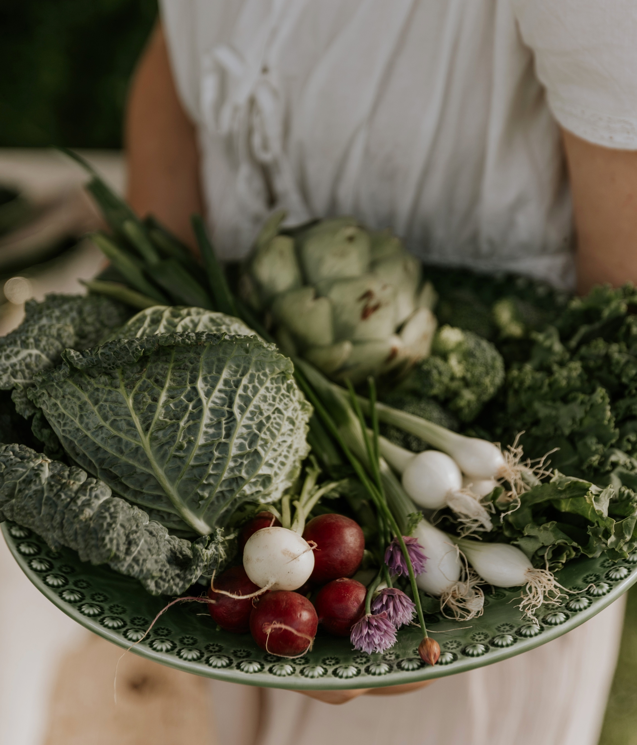 En person holder en grønn tallerken full av grønnsaker