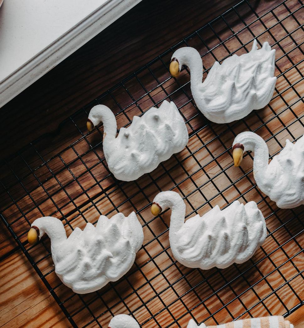 Vita svanformade marängkakor med gula näbbar på ett galler och en randig handduk