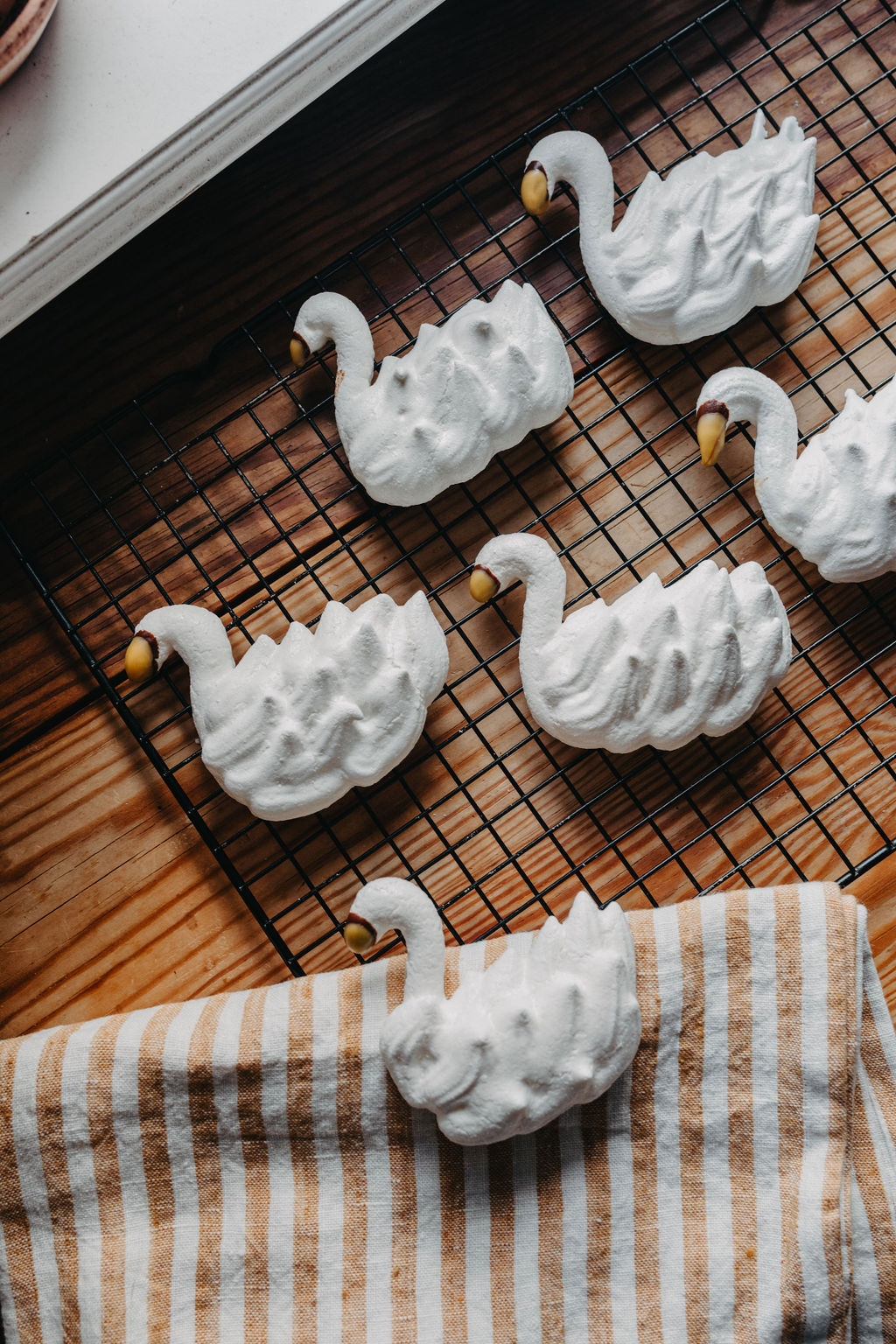 Vita svanformade marängkakor med gula näbbar på ett galler och en randig handduk