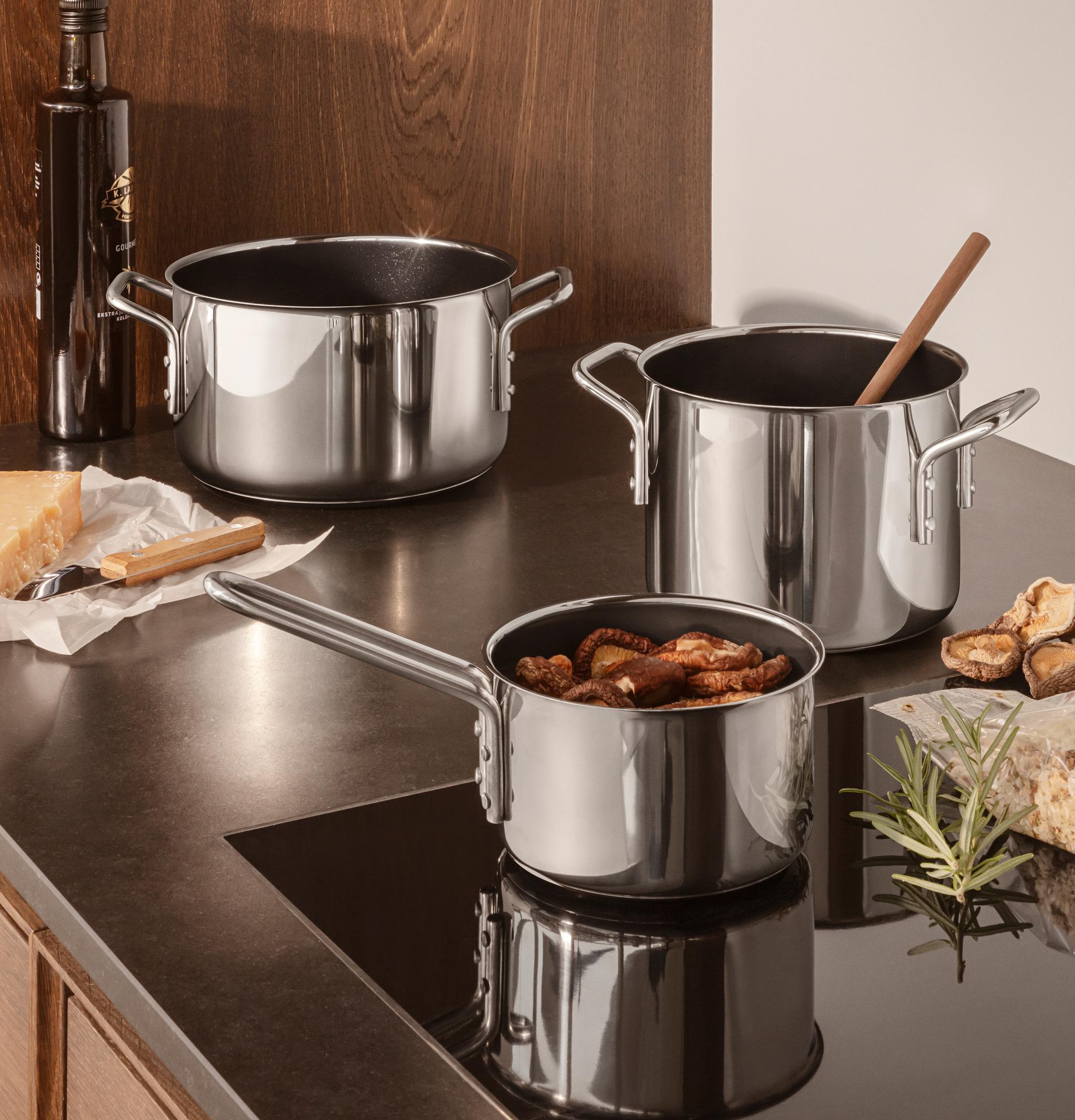 Kolme ruostumattomasta teräksestä valmistettua kattilaa keittiön tiskillä, jossa on juustoa, oliiviöljyä ja kuivattuja sieniä.