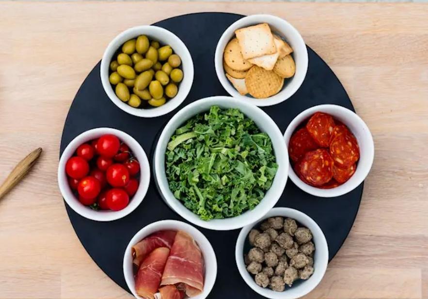 Pöydälle aseteltu runsas valikoima oliiveja, tomaatteja, lehtikaalia, juustoja, leikkeleitä ja muita tapas-herkkuja.